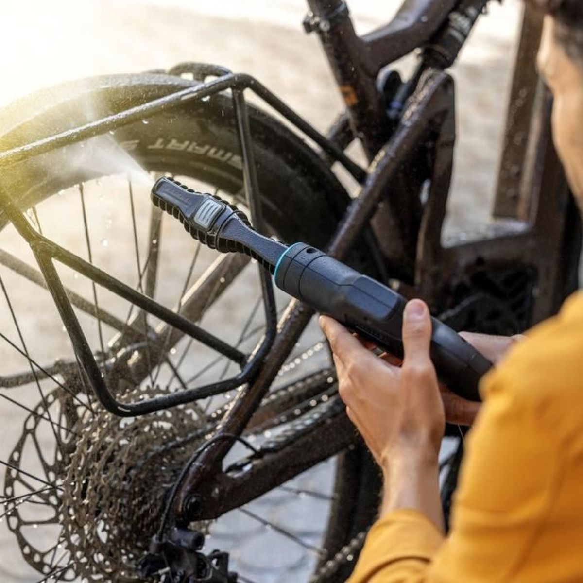 Une personne lave un vélo avec un nettoyeur haute pression noir, l'eau pulvérise.