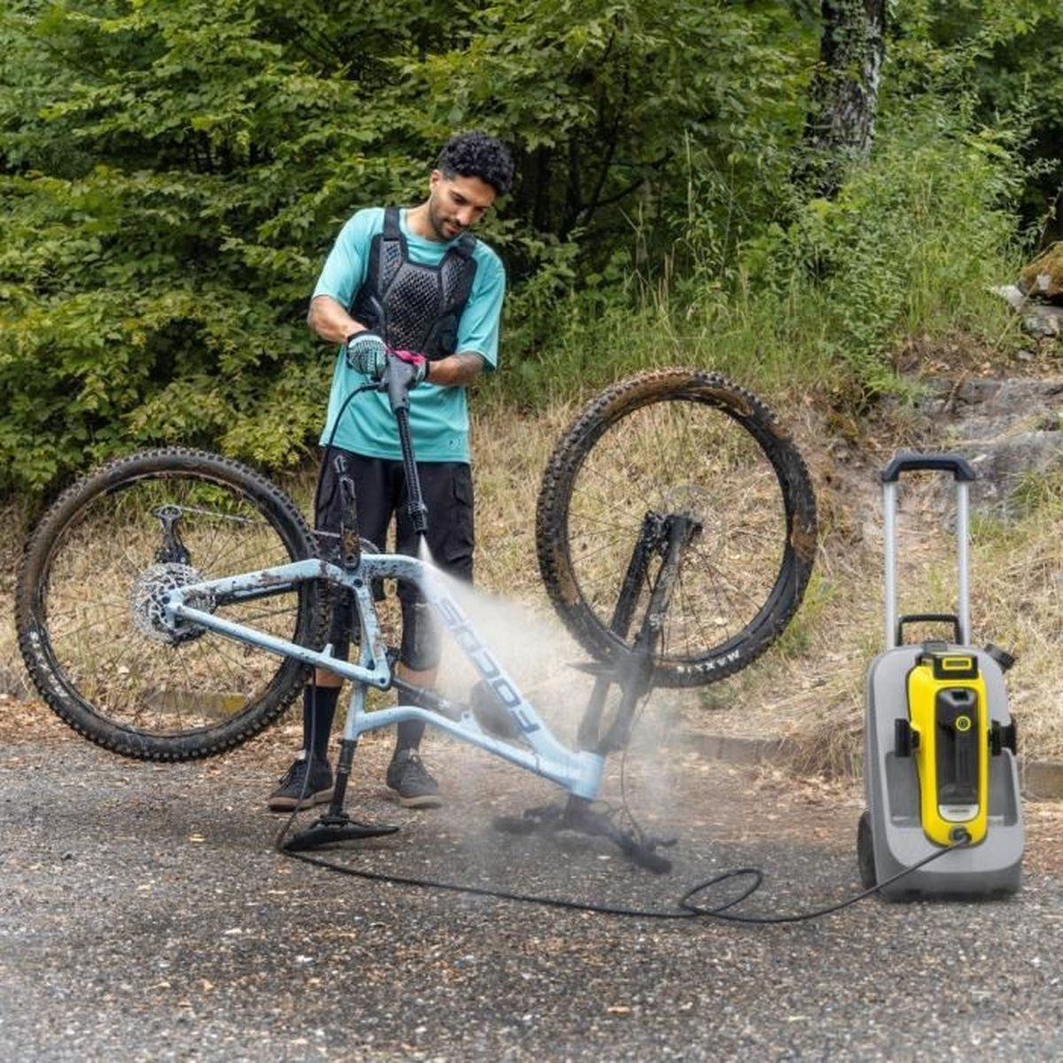 Une personne utilise un nettoyeur haute pression pour nettoyer un VTT sur un chemin de gravier.