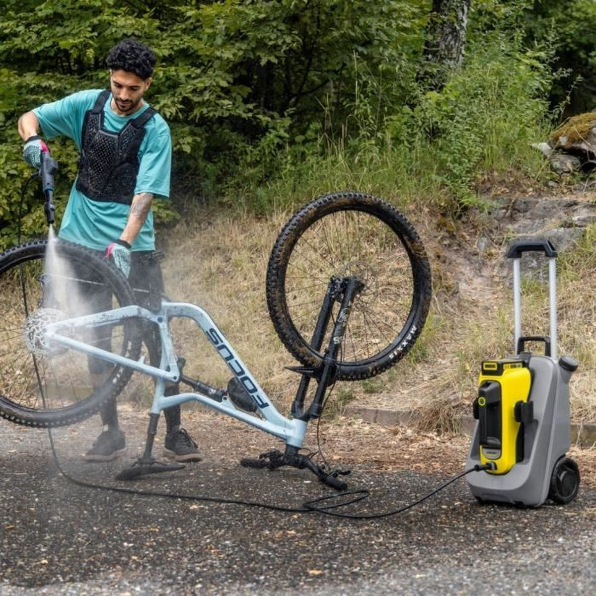Un homme lavant un VTT avec un nettoyeur haute pression à l'extérieur.