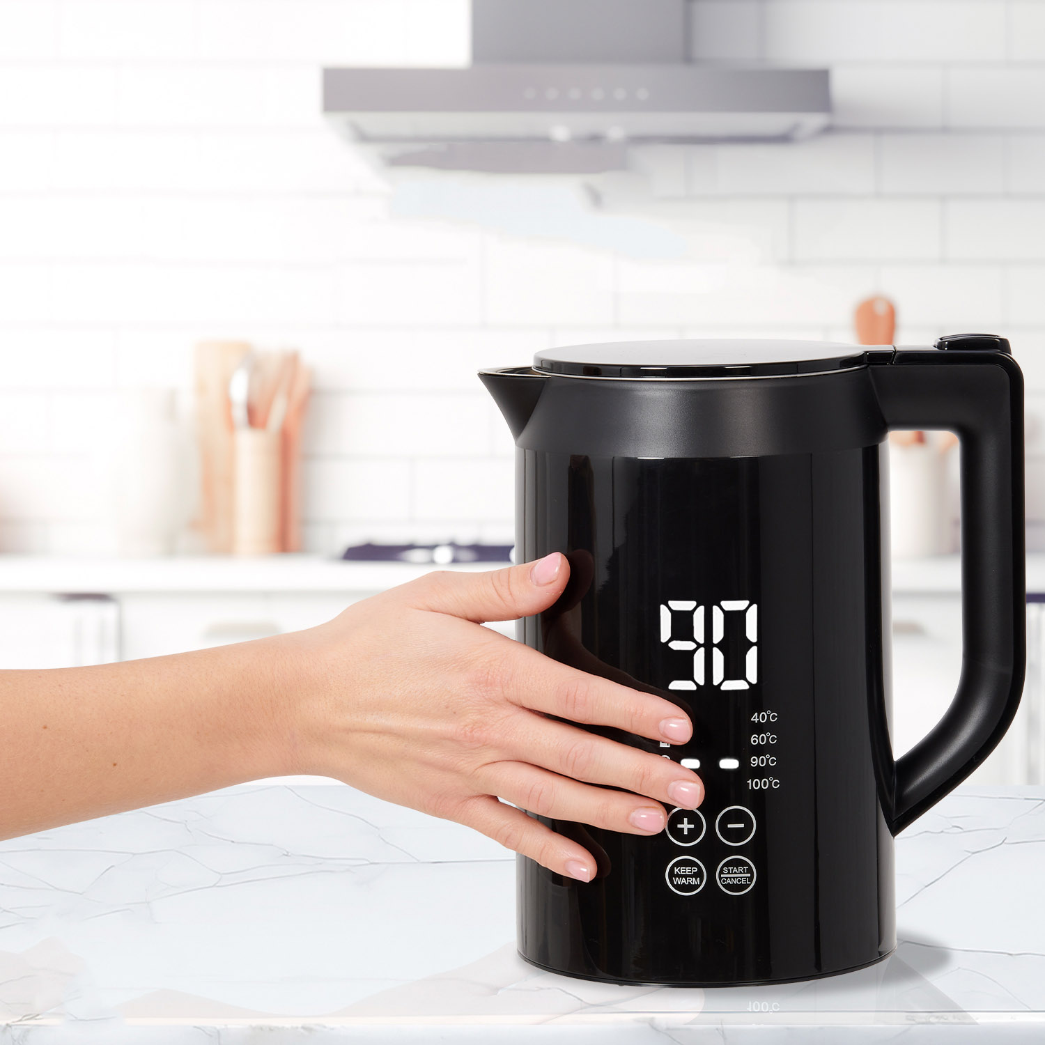 A hand touching a black kettle with a digital display showing 90 degrees Celsius and temperature settings.