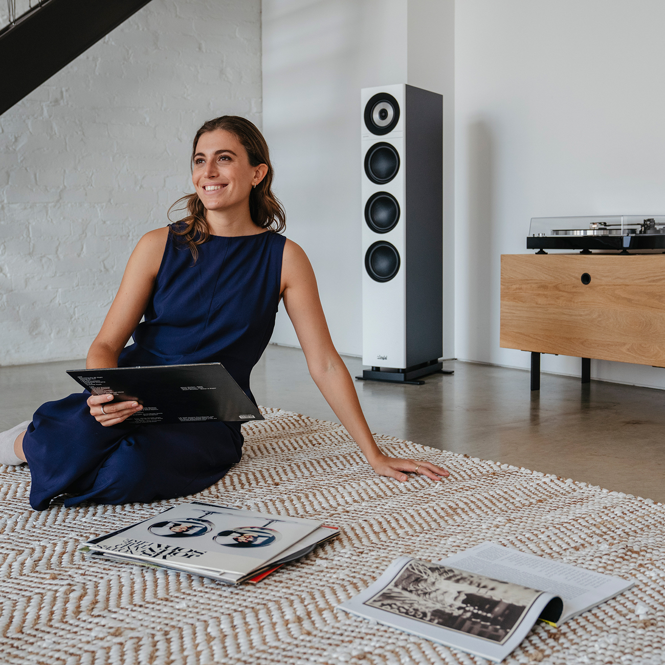 Een vrouw zit op de grond met een lp-album. Een hoge luidspreker en een houten kast op de achtergrond.