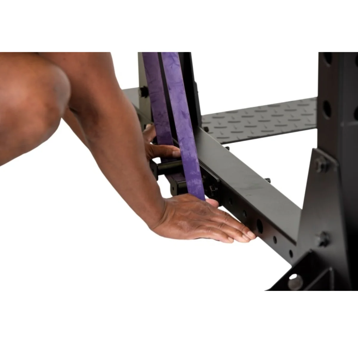 Een persoon bevestigt een paarse weerstandsband aan een zwart power rack, close-up van handen en het rek.