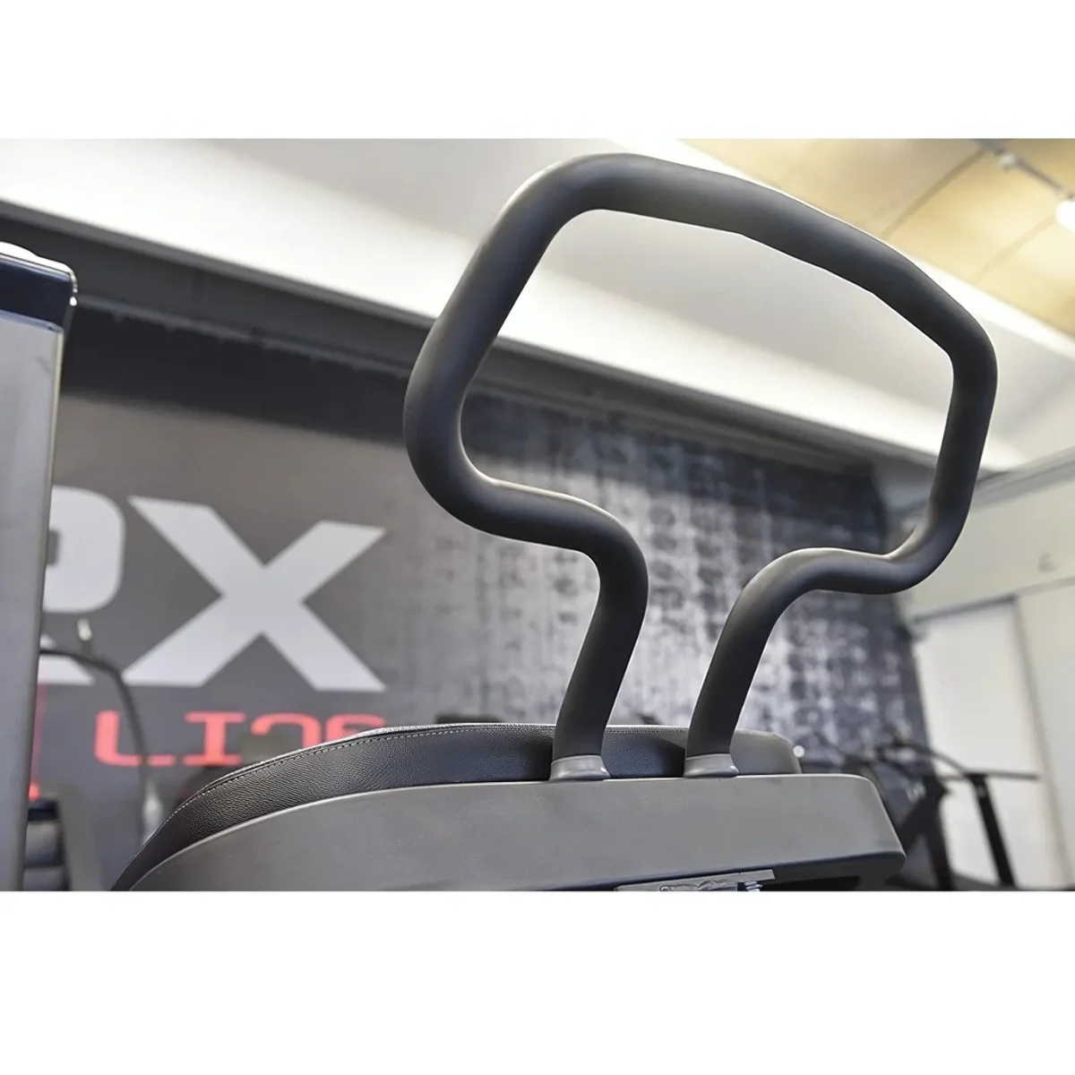 Handvat van fitnessapparatuur, gebogen en zwart, bevestigd aan een machine. De achtergrond is wazig.