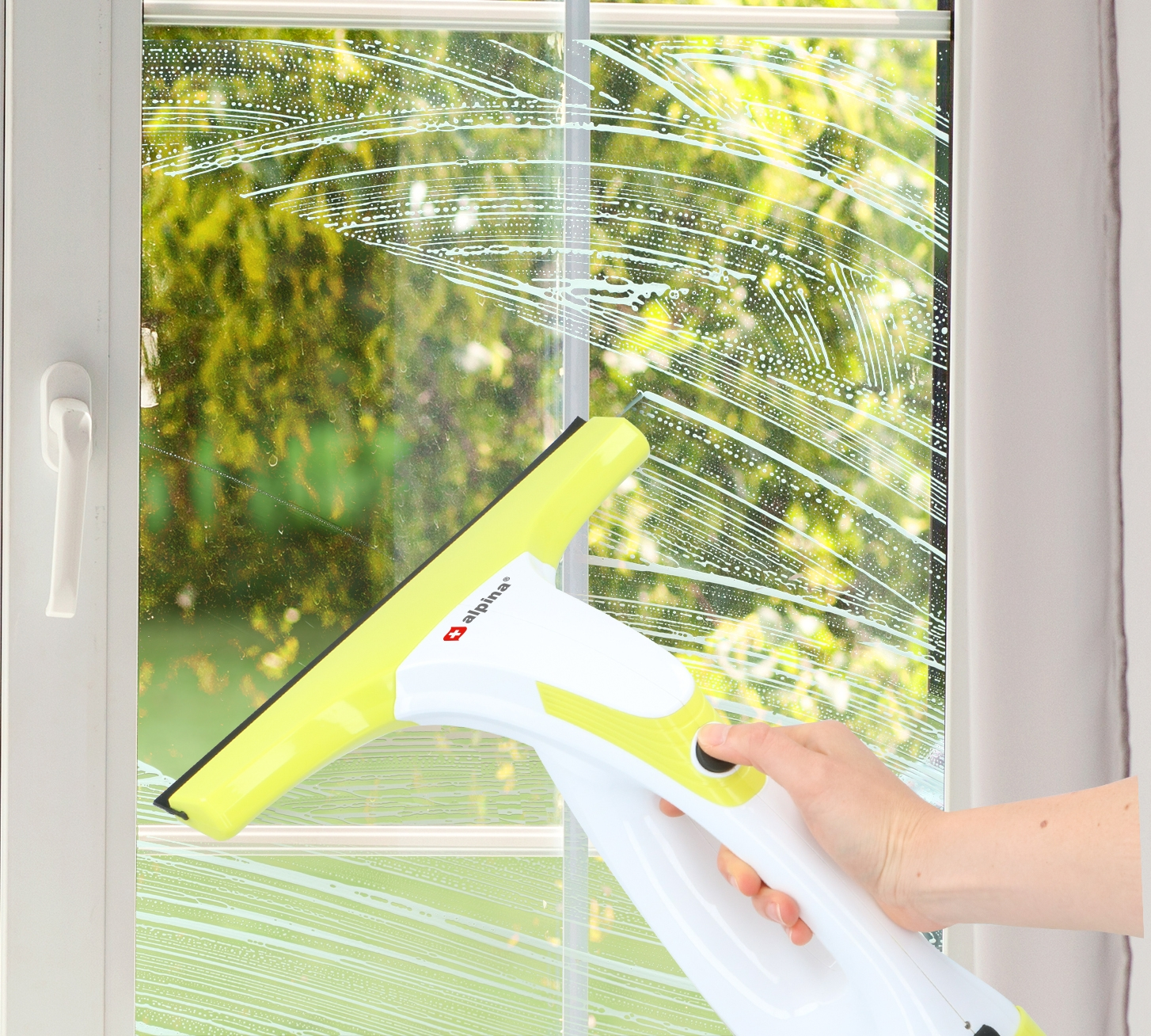 Eine Hand benutzt einen Fensterreiniger, um ein Fenster zu reinigen, mit einem grün-weißen Reiniger.