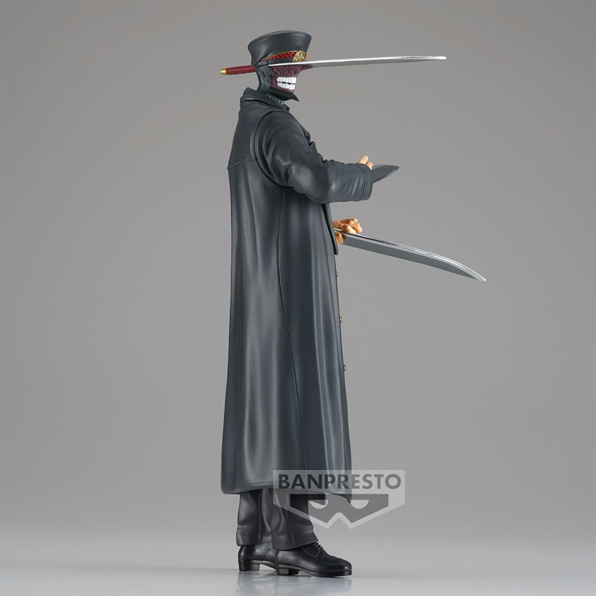 Figur eines Mannes in einem schwarzen Mantel mit Schwertern in Händen und Mund. Banpresto-Logo unten.