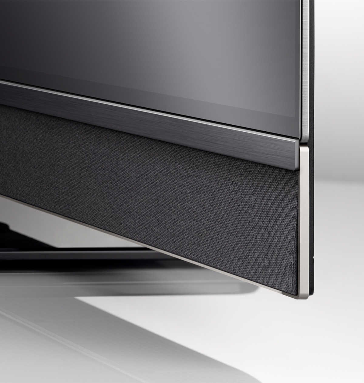 Primo piano del bordo inferiore di un televisore con una soundbar rivestita in tessuto e finiture argentate.