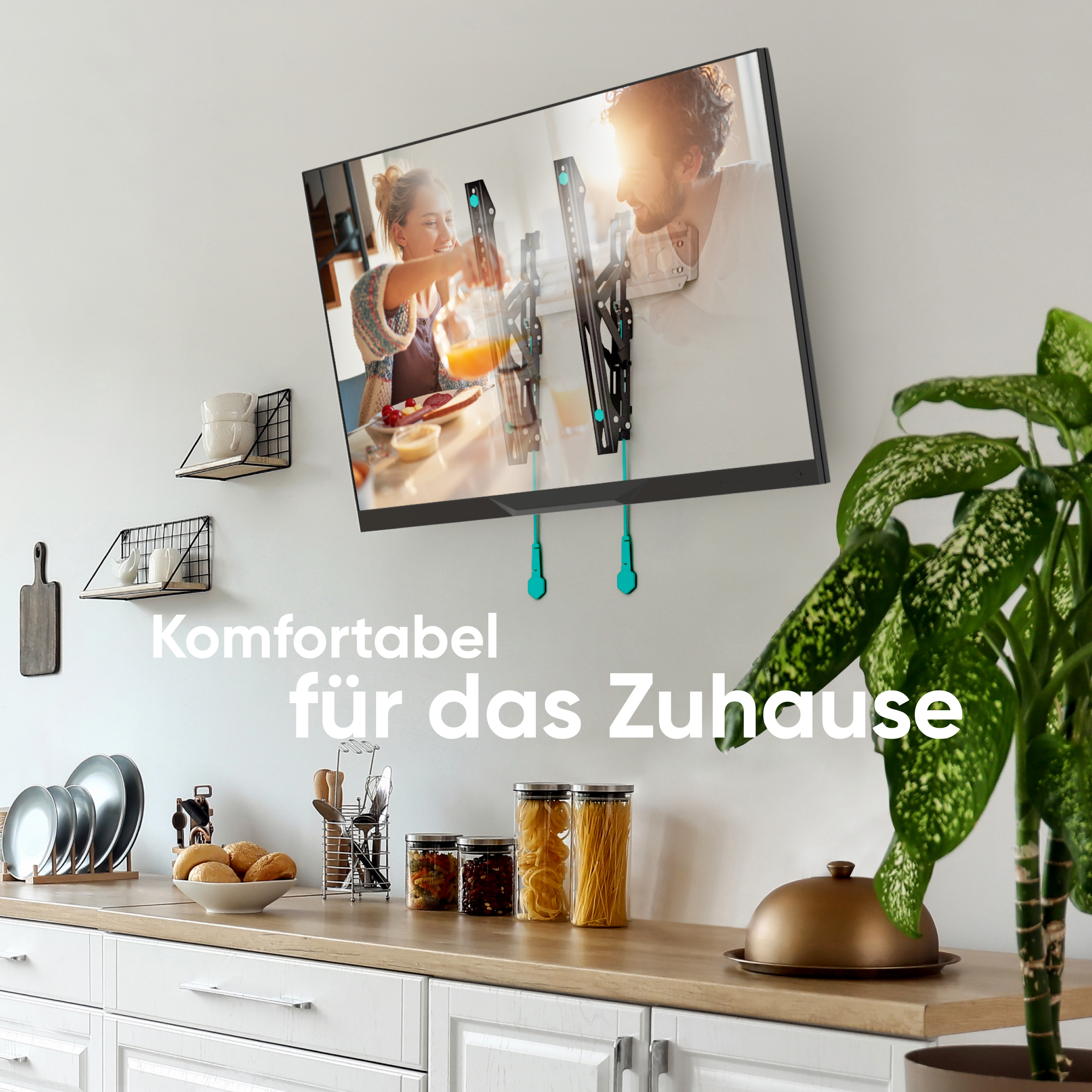 Ein Fernseher zeigt ein Paar in der Küche. Eine grüne Pflanze im Vordergrund, darunter ein weißer Schrank.