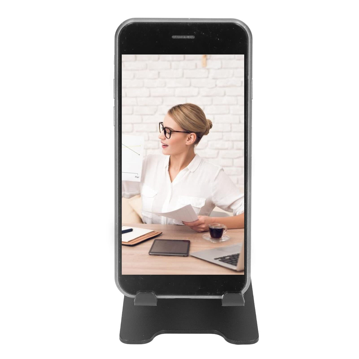 Ein Smartphone in einem Ständer, das eine Frau zeigt, die Papiere betrachtet. Auf dem Schreibtisch liegen Laptop, Tablet und Kaffee.