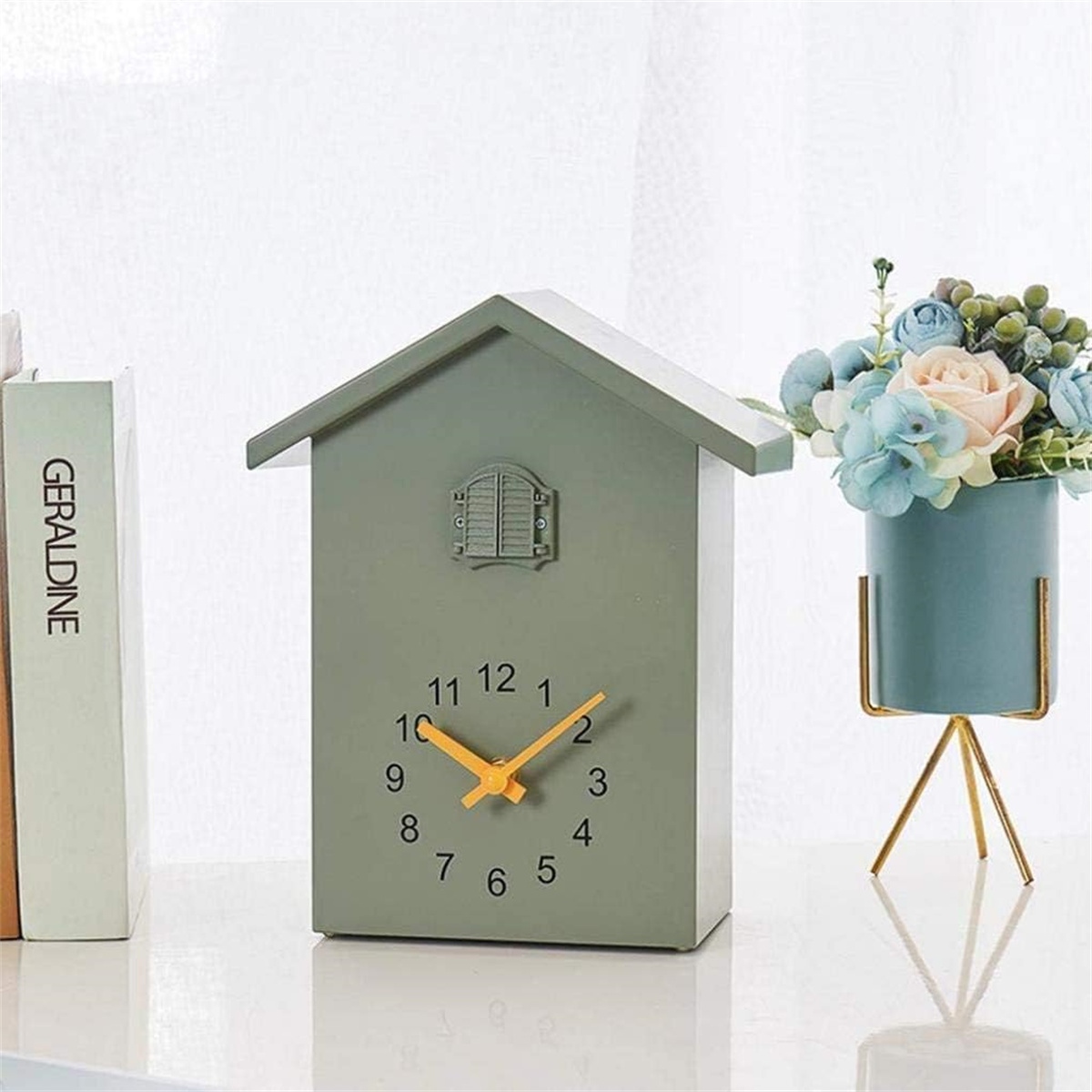 Eine grüne, vogelhausförmige Uhr mit einer hellblauen Vase mit Blumen.