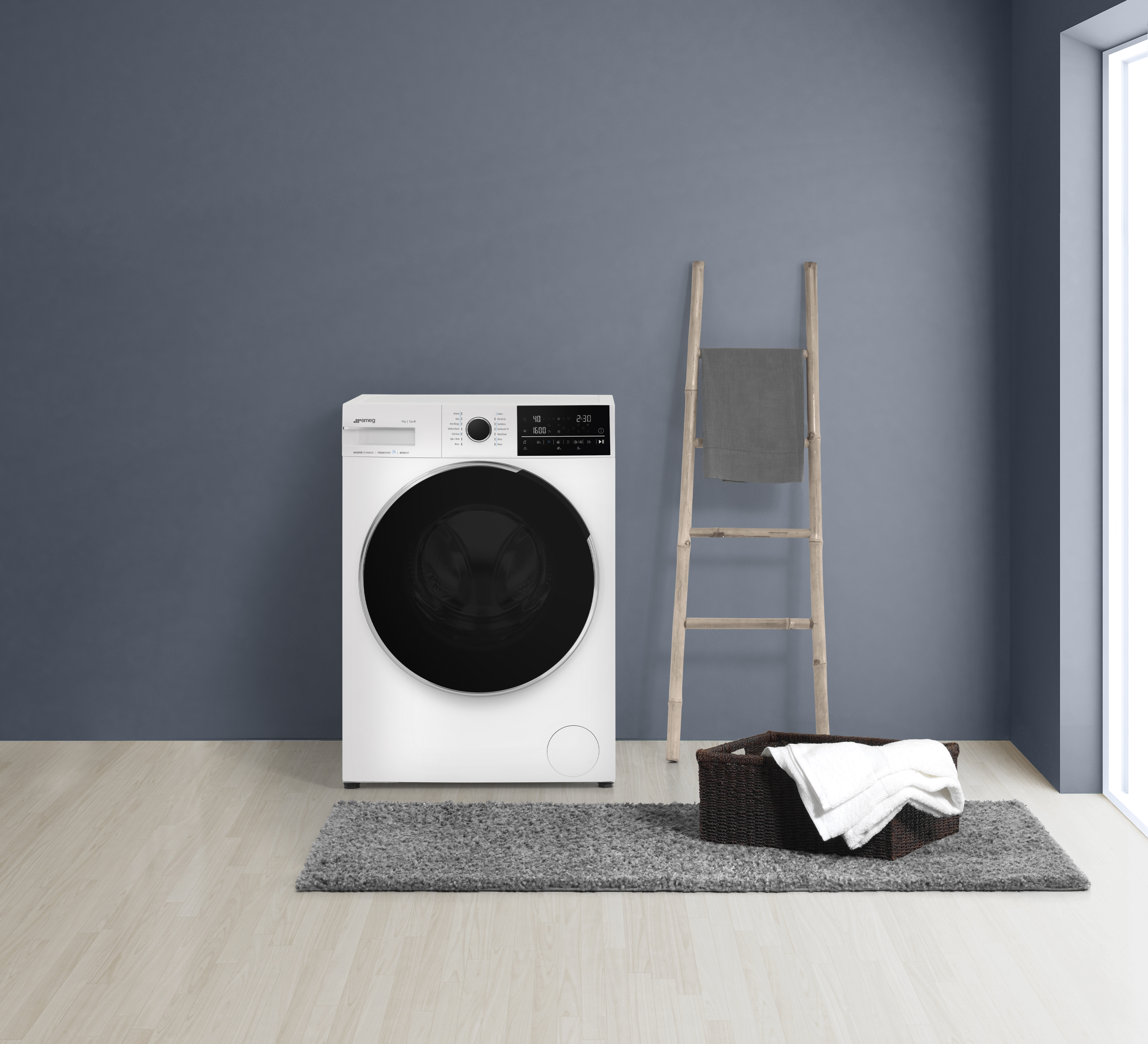 Biała pralka, dywan, kosz z ręcznikami i drewniana drabina na tle niebieskiej ściany.