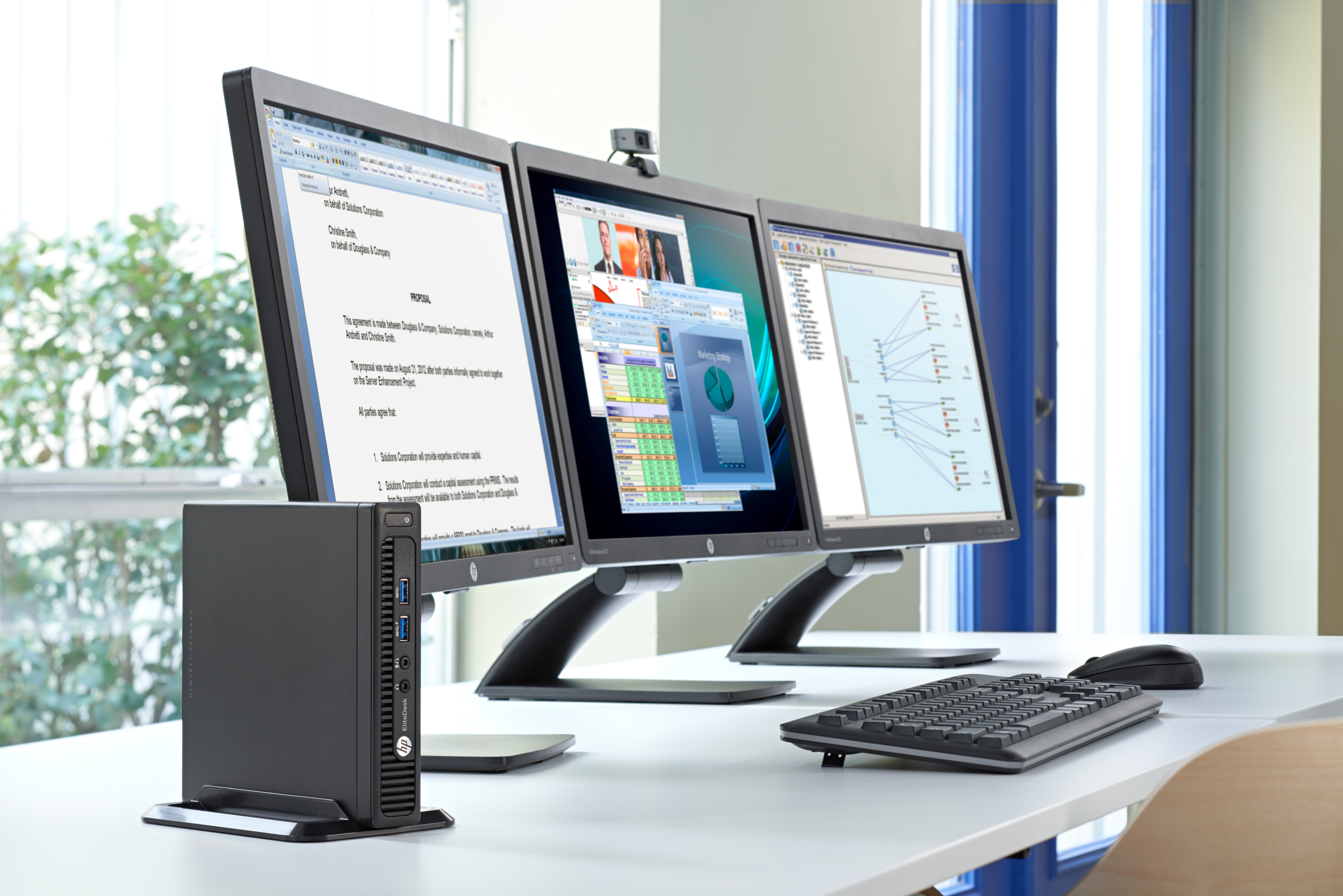 Tre monitor HP che mostrano documenti e interfacce software su una scrivania con un computer.