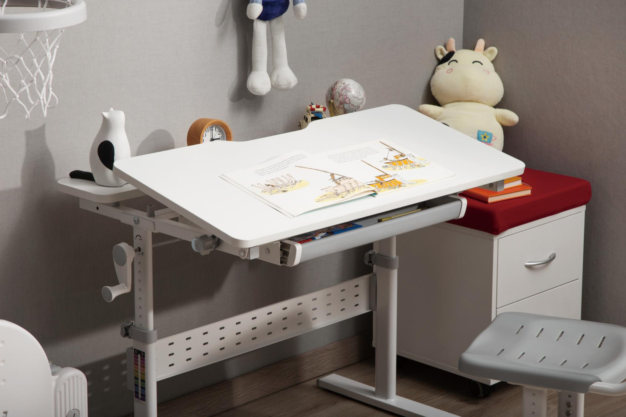 Een verstelbaar wit bureau voor kinderen met schoolspullen. Achtergrond is een lichtgrijze muur en een grijze stoel.