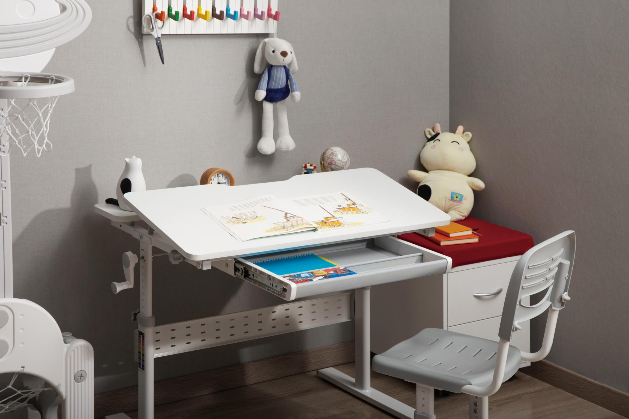 Kinderbureau met speelgoed, boeken en stoel. De kamer heeft een grijze muur en decoraties.