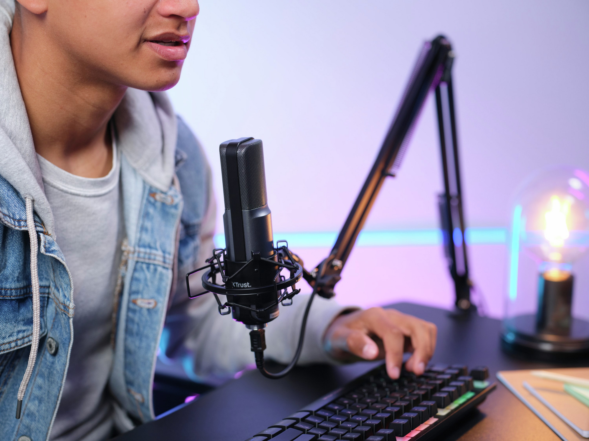 Ein Mann mit Mikrofon, Tastatur und Monitor, eingerichtet für Streaming.