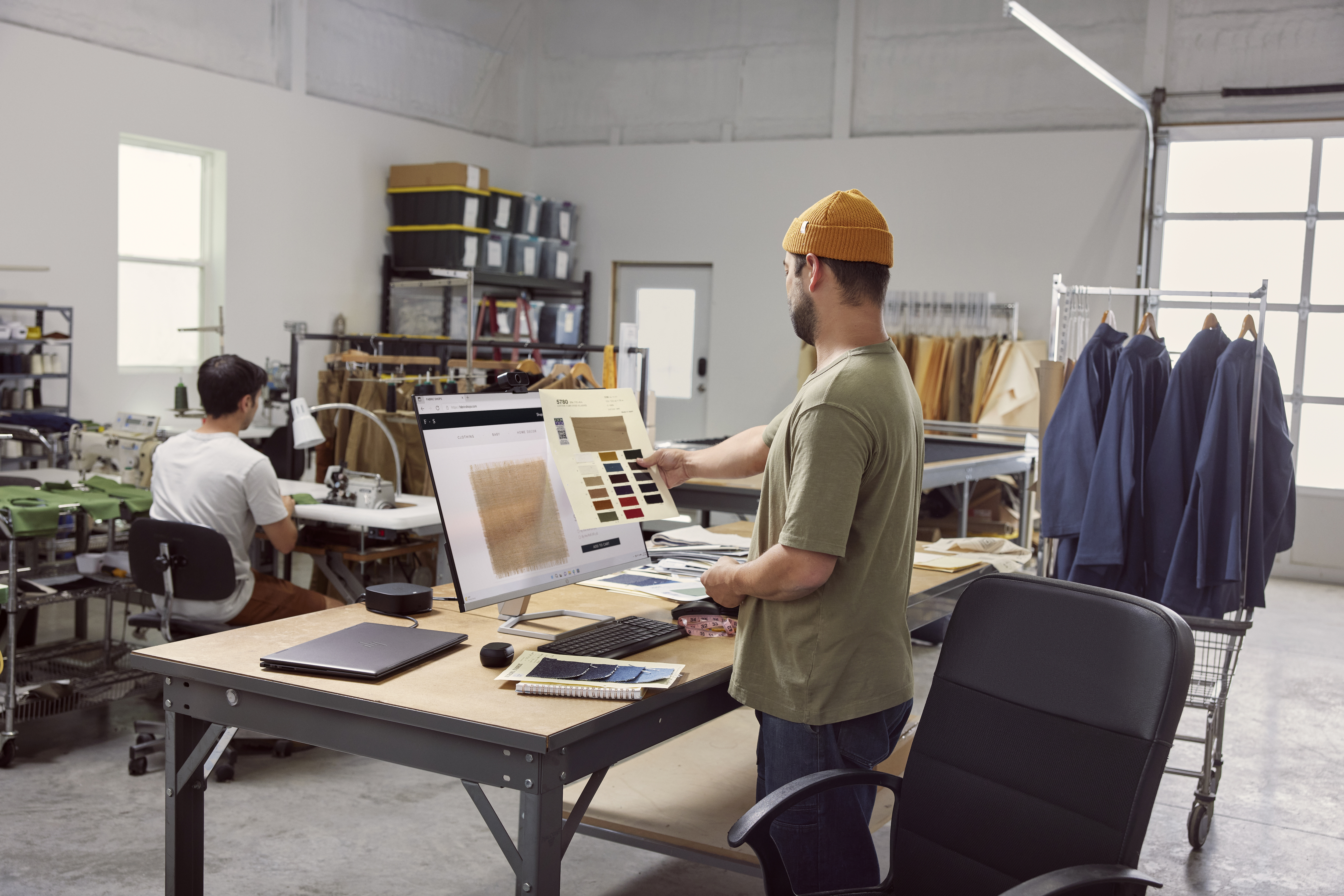 Dwie osoby w warsztacie. Jedna trzyma wzorniki kolorów w pobliżu ekranu komputera.