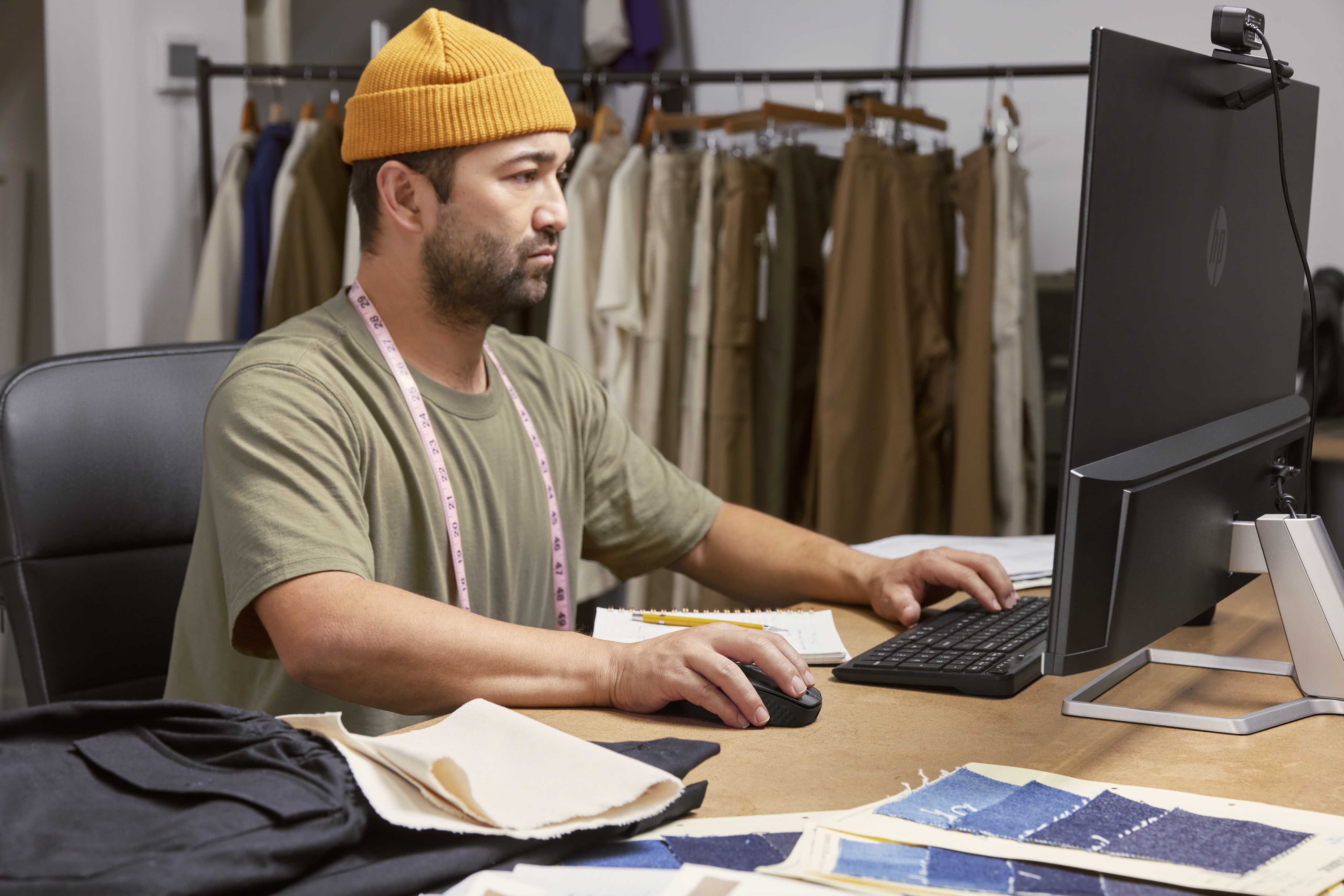 Mężczyzna w pomarańczowym kapeluszu używający komputera z monitorem i klawiaturą.