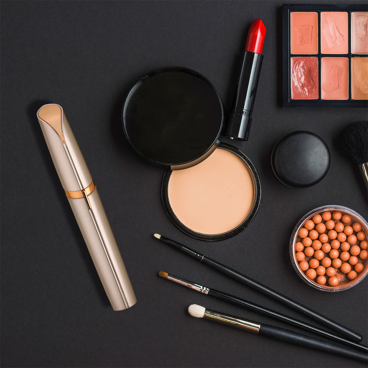 Make-up-Produkte auf schwarzer Oberfläche: Pinsel, Lippenstift, Puder und Kompaktpuder.