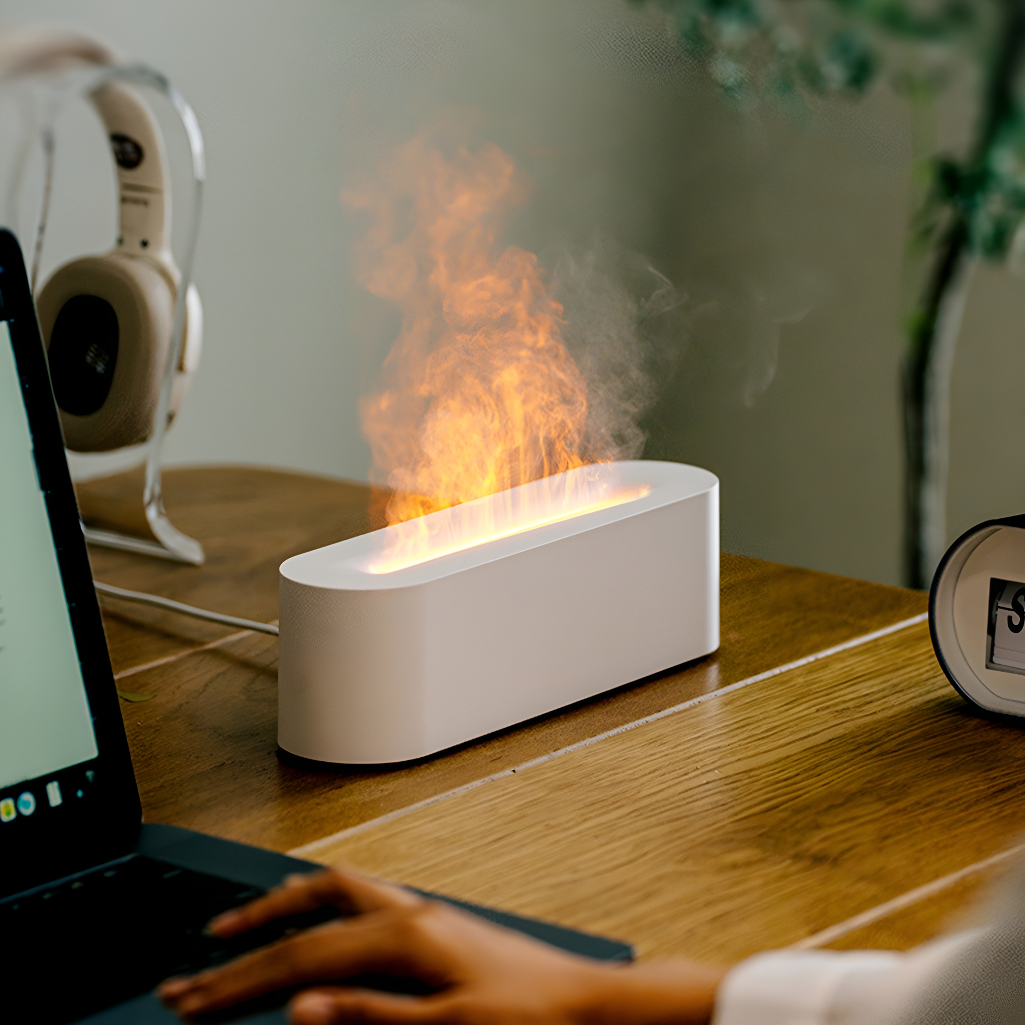 Weißes Gerät mit Flammeneffekt auf Holzschreibtisch. Flammen und Rauch sichtbar. Laptop und andere Objekte im Hintergrund.