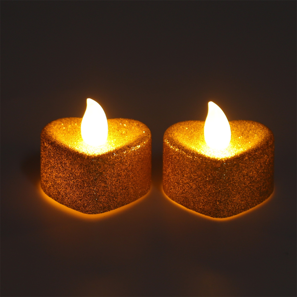 Zwei herzförmige, goldglitzernde Kerzen mit hellen, gelben Flammen auf dunklem Hintergrund.