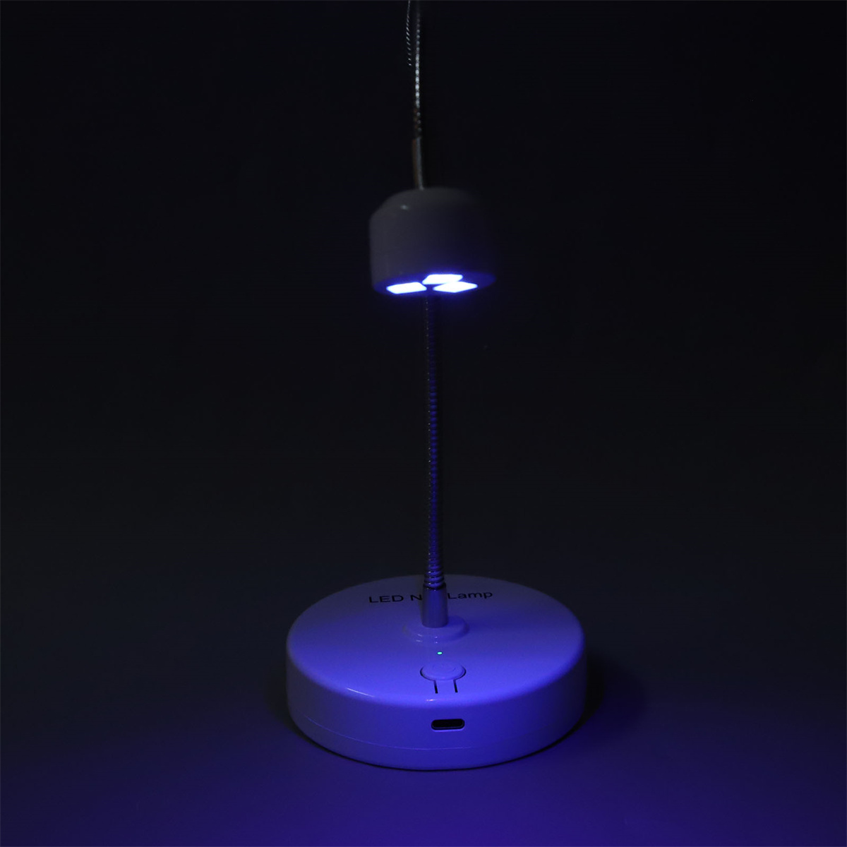 Eine weiße LED-Nagellampe mit flexiblem Arm, Sockel blau beleuchtet. Dunkler Hintergrund.