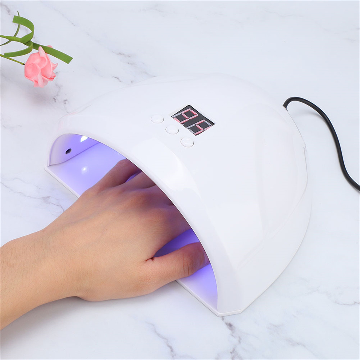 Eine Hand befindet sich in einem weißen Nageltrockner mit Digitalanzeige. Eine rosa Blume daneben.