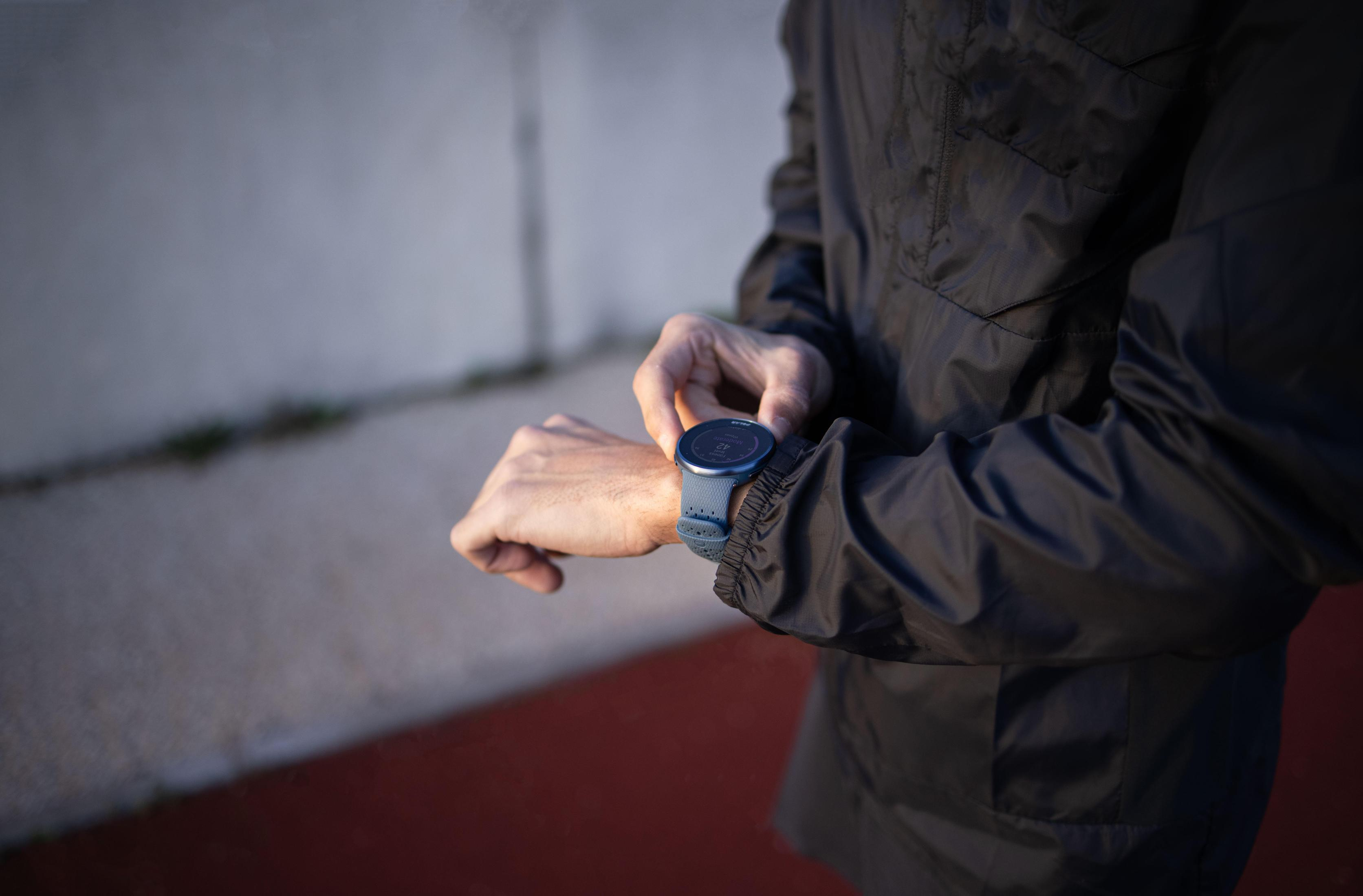 Osoba nosząca niebieski smartwatch, sprawdzająca czas lub dane na ekranie zegarka.