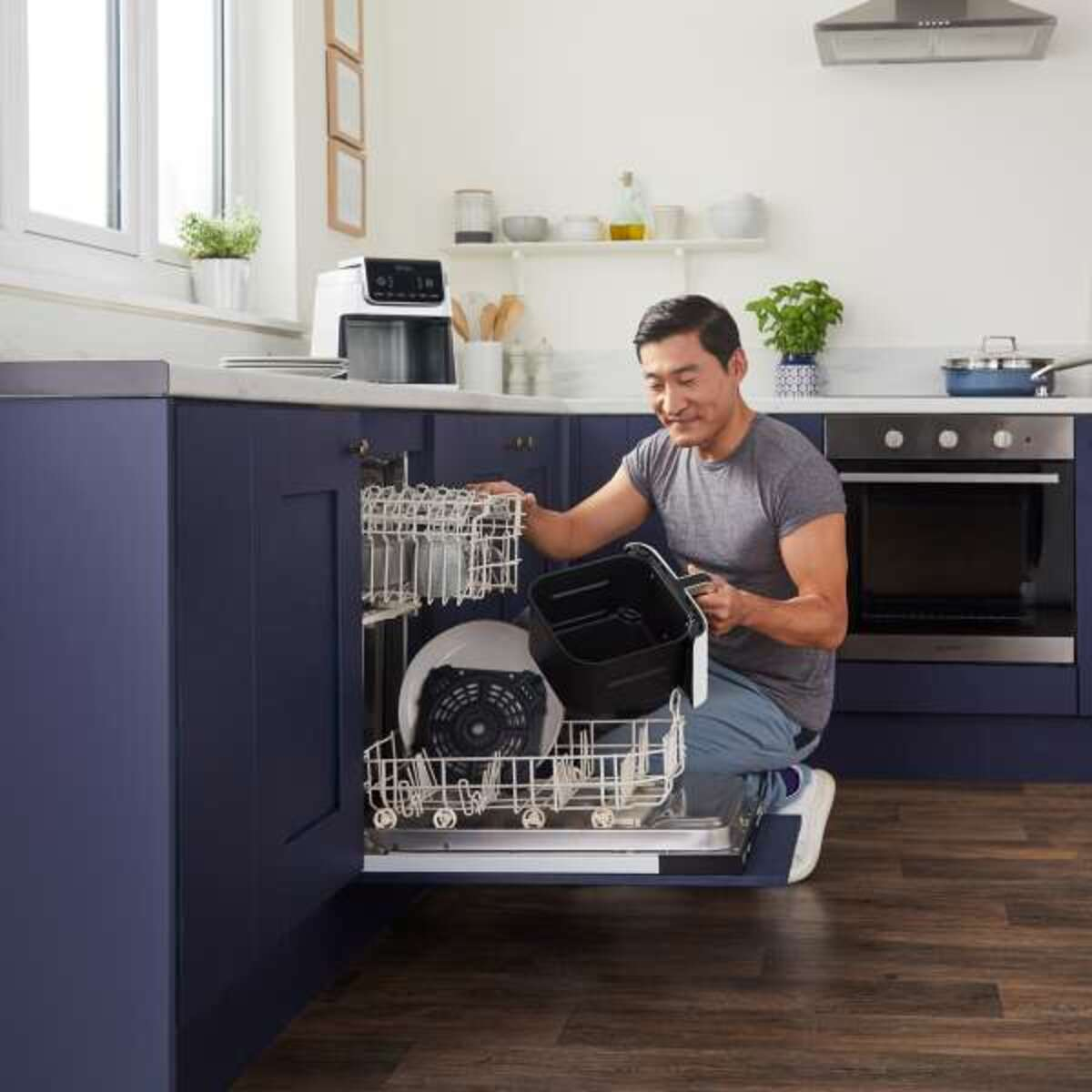 Mężczyzna wkładający kosz frytkownicy do zmywarki w niebiesko-białej kuchni.