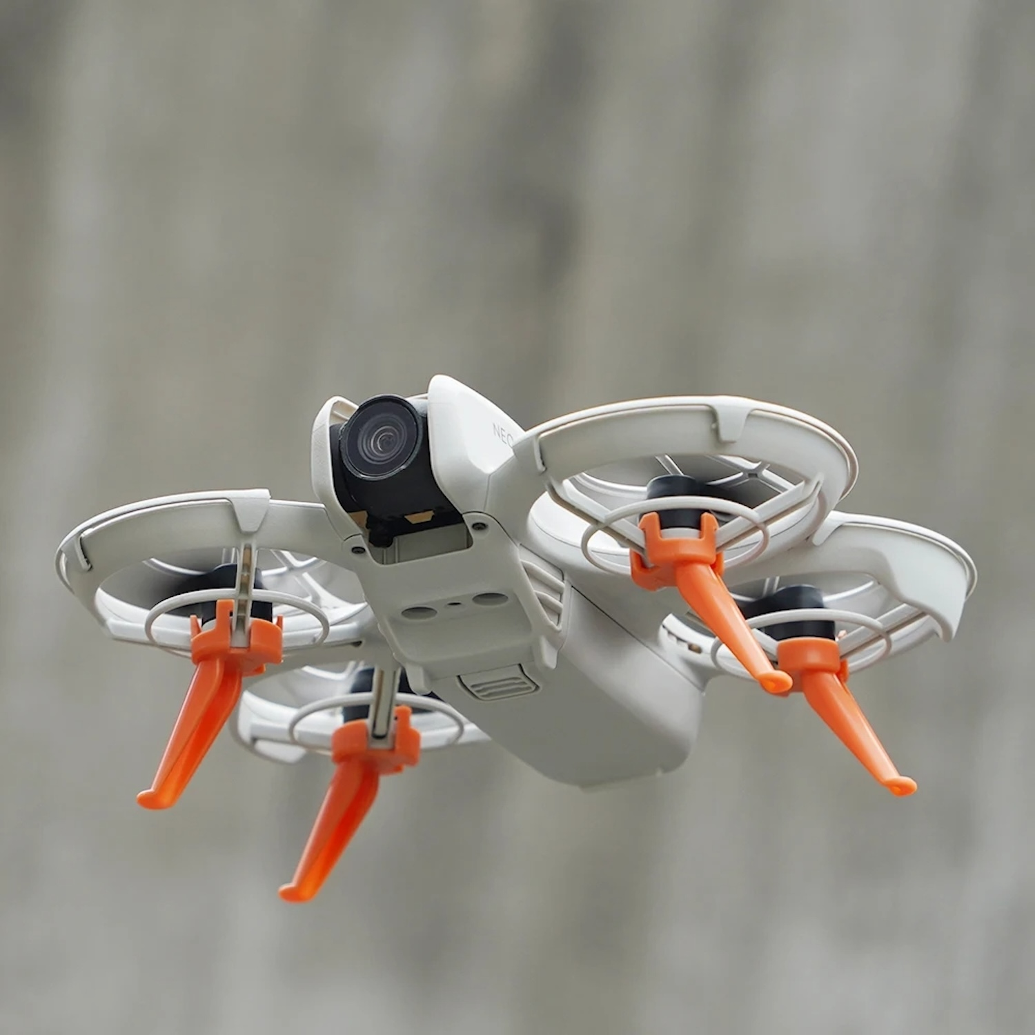 Un dron volando, con cuerpo blanco, patas naranjas y una cámara.