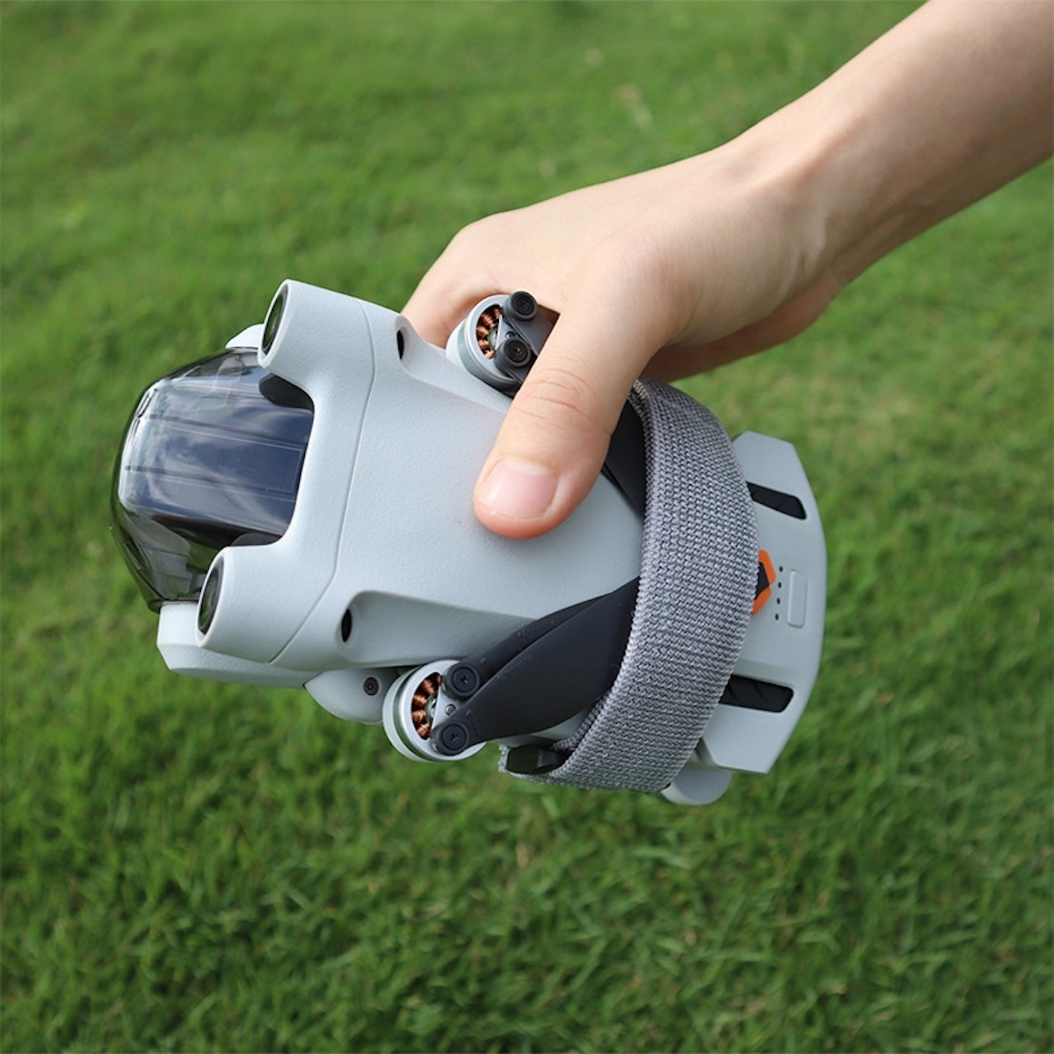 Un drone grigio tenuto in mano, contro l'erba verde. Il drone ha un cinturino grigio.