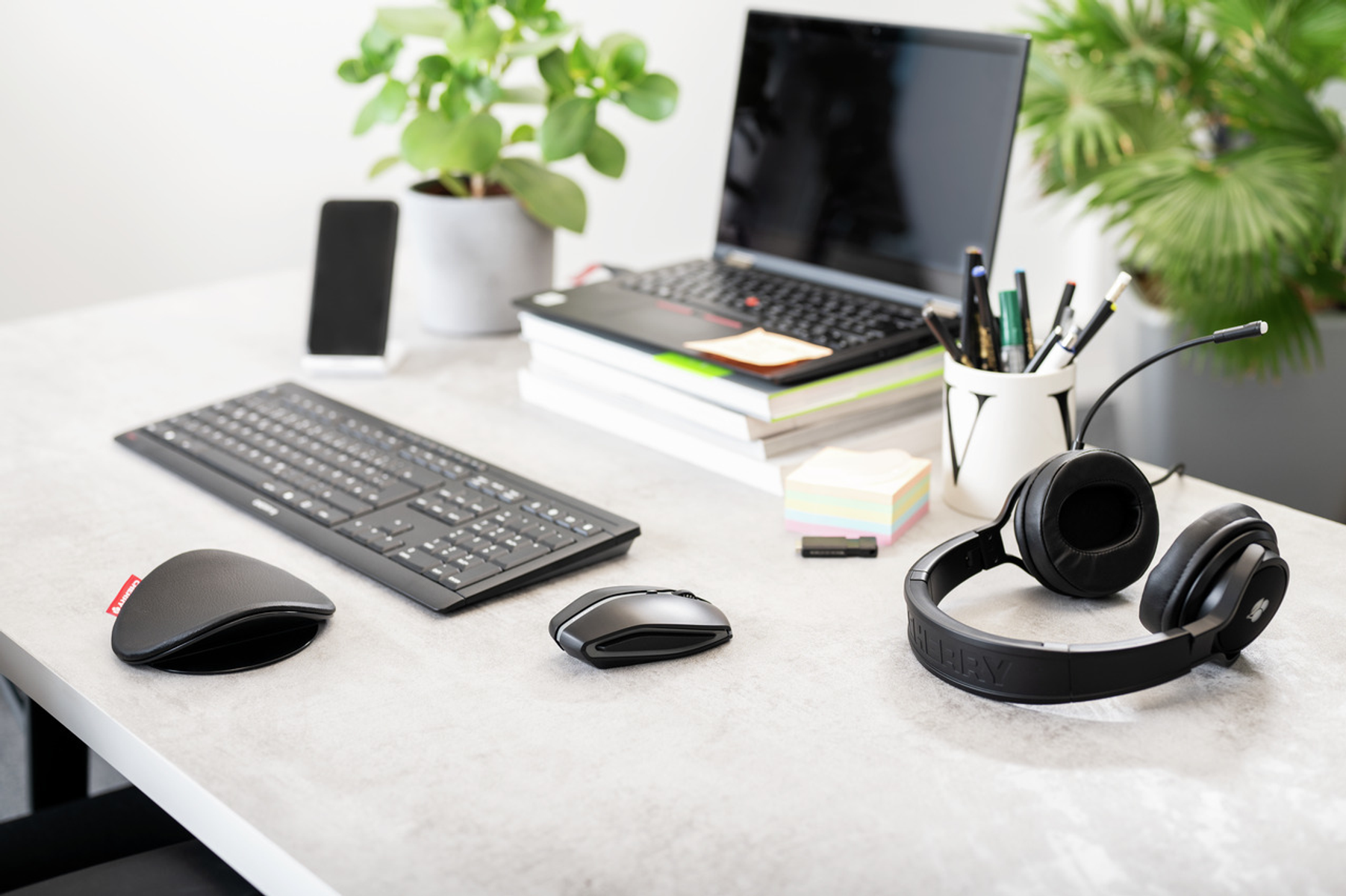 Office desk with laptop, keyboard, mouse, phone, headphones, pens, and a plant. All in view.