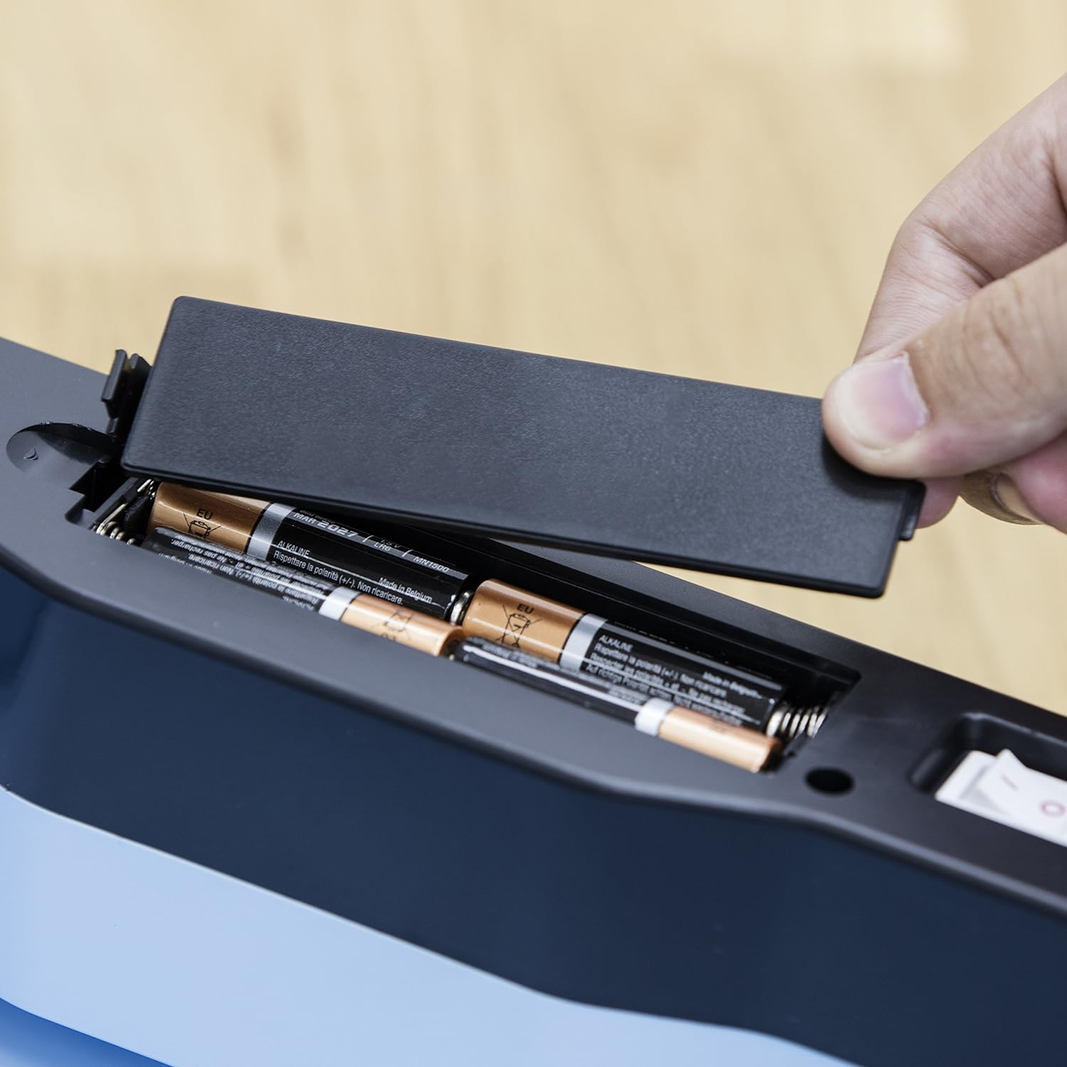 Hand öffnet ein Batteriefach. Batterien sichtbar, Deckel an der Seite, Nahaufnahme.