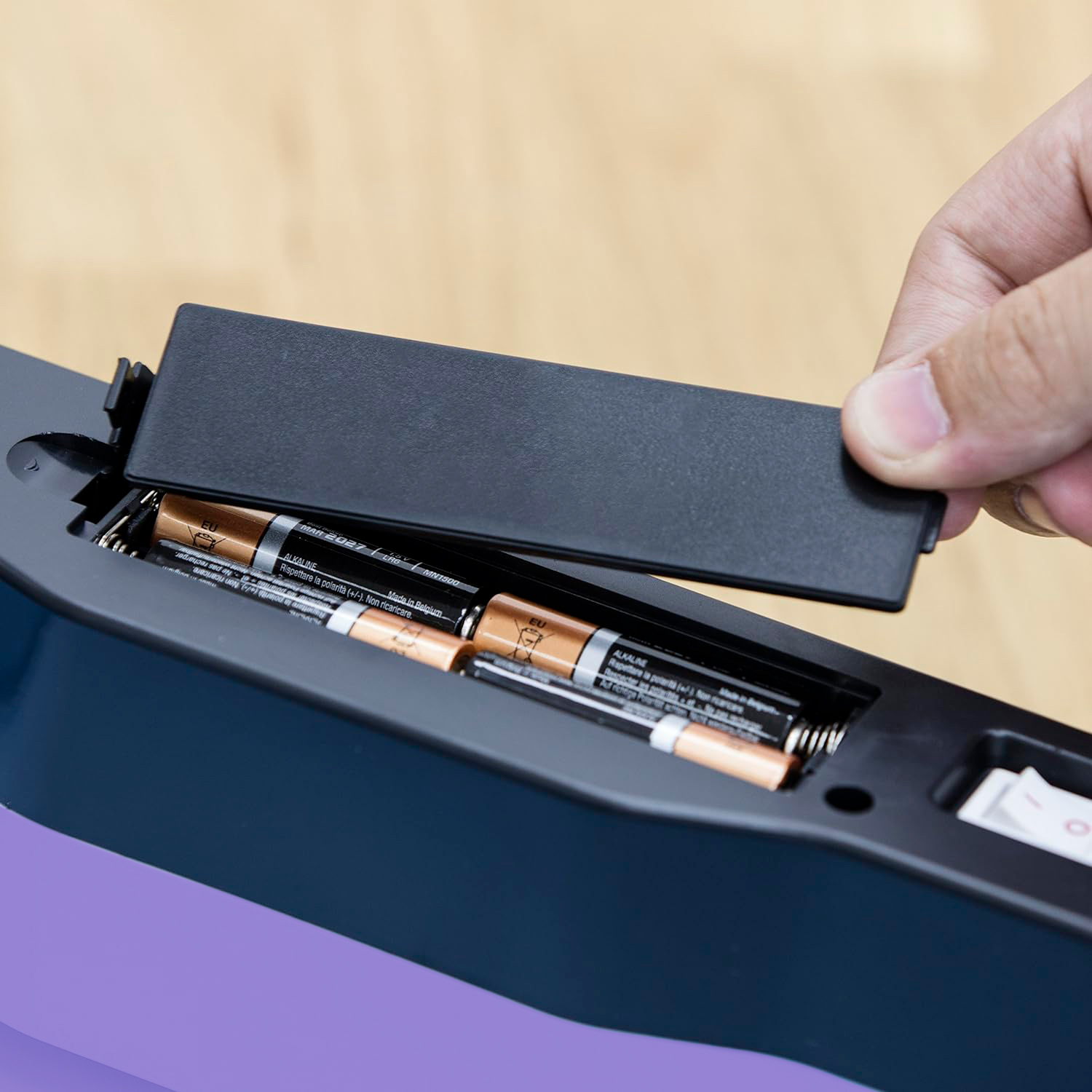 Una mano abre un compartimento de batería de un dispositivo electrónico azul oscuro y púrpura.