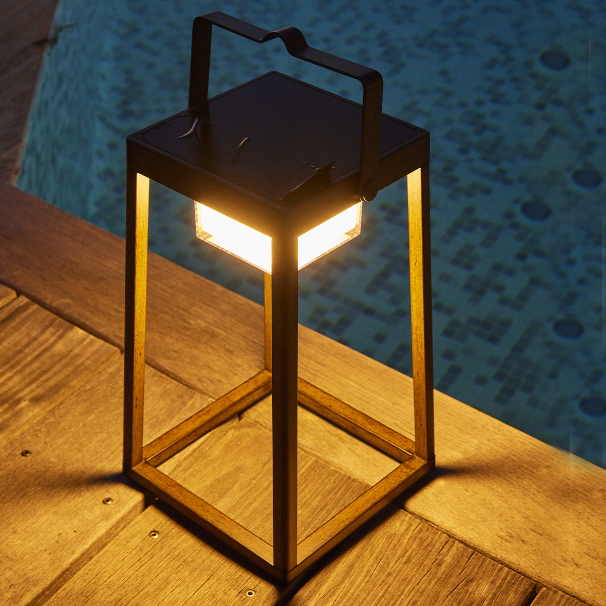 Eine schwarze Außenlaterne auf einem Holzdeck neben Wasser, mit einer beleuchteten Lichtquelle im Inneren.