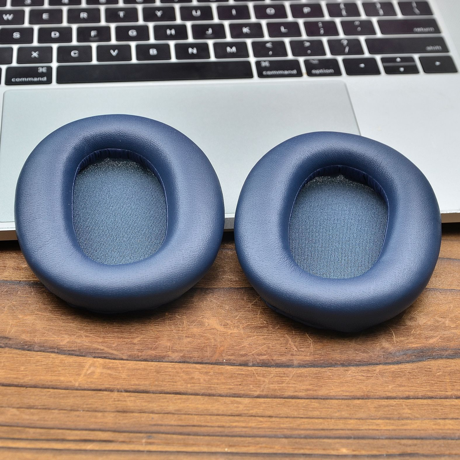 Dwie niebieskie nauszne poduszki słuchawkowe na drewnianej powierzchni. Klawiatura w tle.