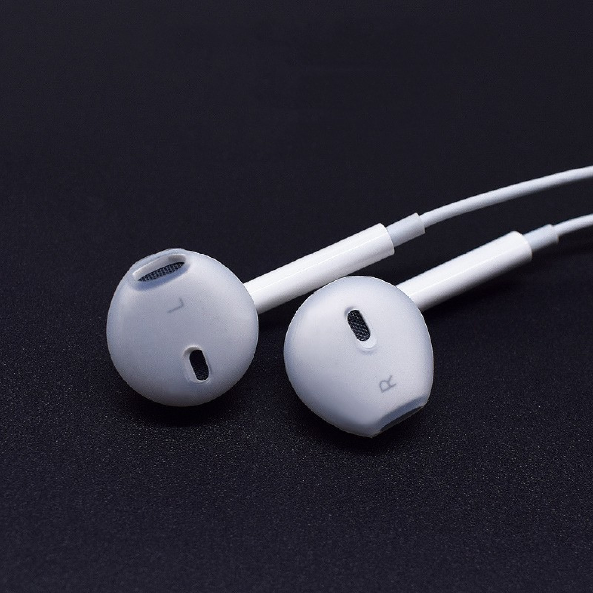 Auricolari bianchi con punte grigie su superficie nera. Gli auricolari sono rotondi e collegati da un cavo bianco.