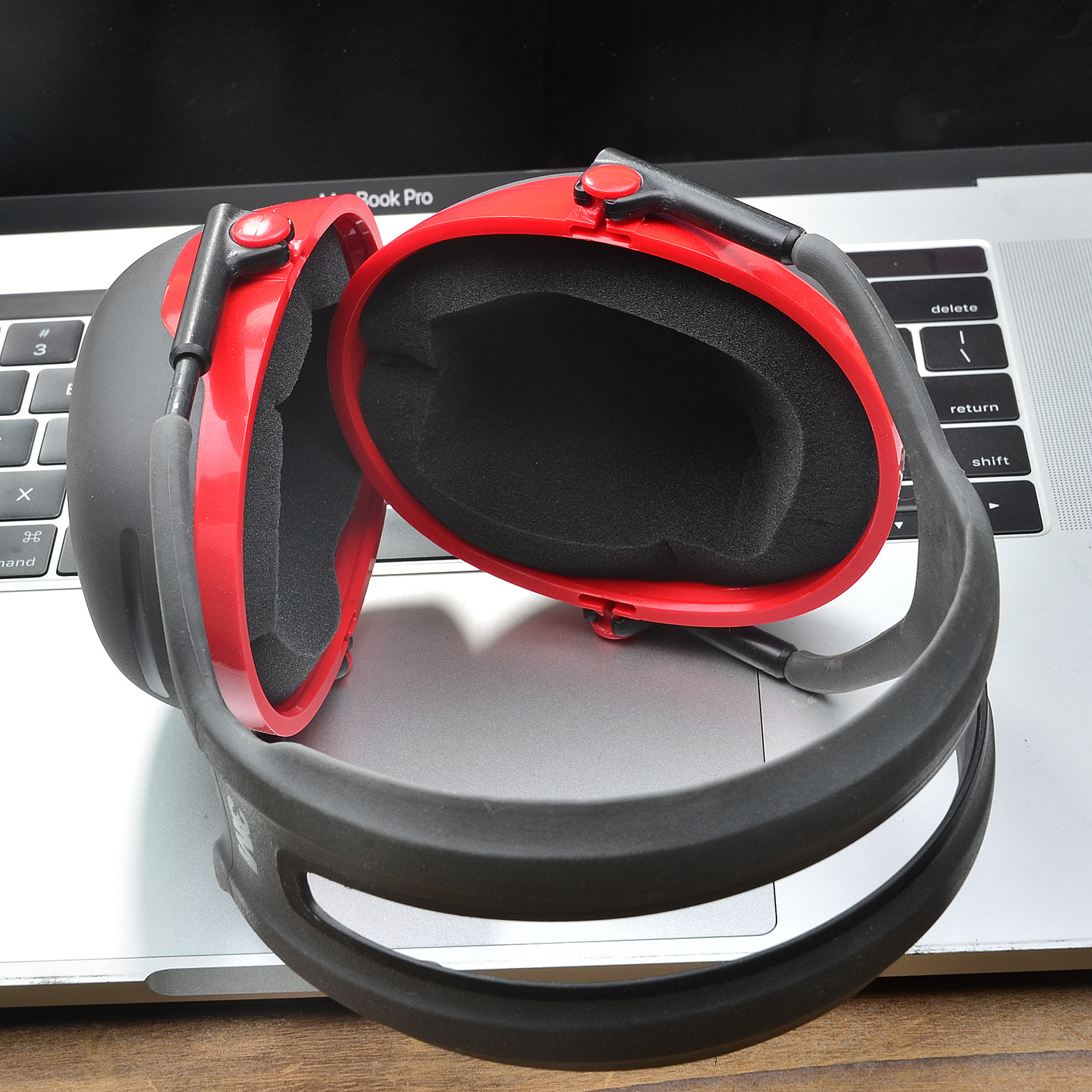 Czerwone i czarne nauszniki leżą na klawiaturze laptopa. Klawiatura jest srebrna.