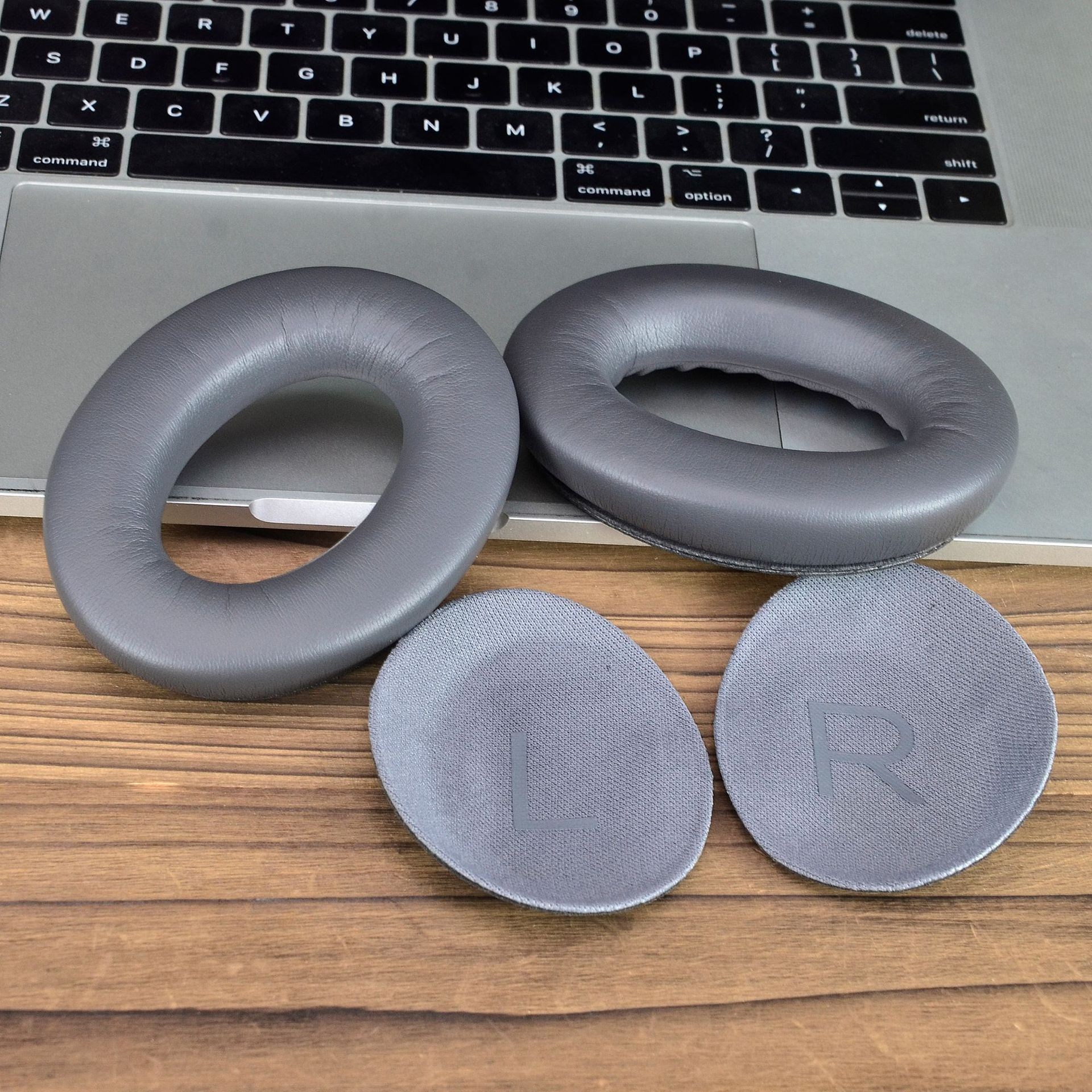 Twee grijze oorkussens en twee kleine grijze pads met de letter 'R' op een houten oppervlak.
