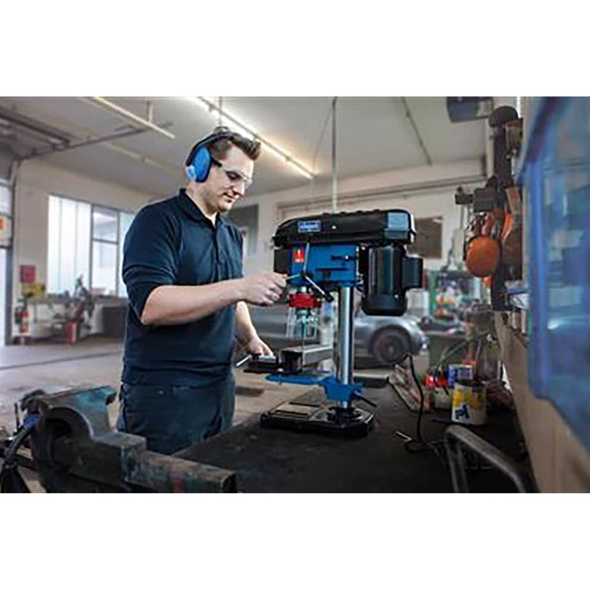 Mężczyzna w okularach ochronnych i ochronie słuchu używa niebiesko-czarnej wiertarki.