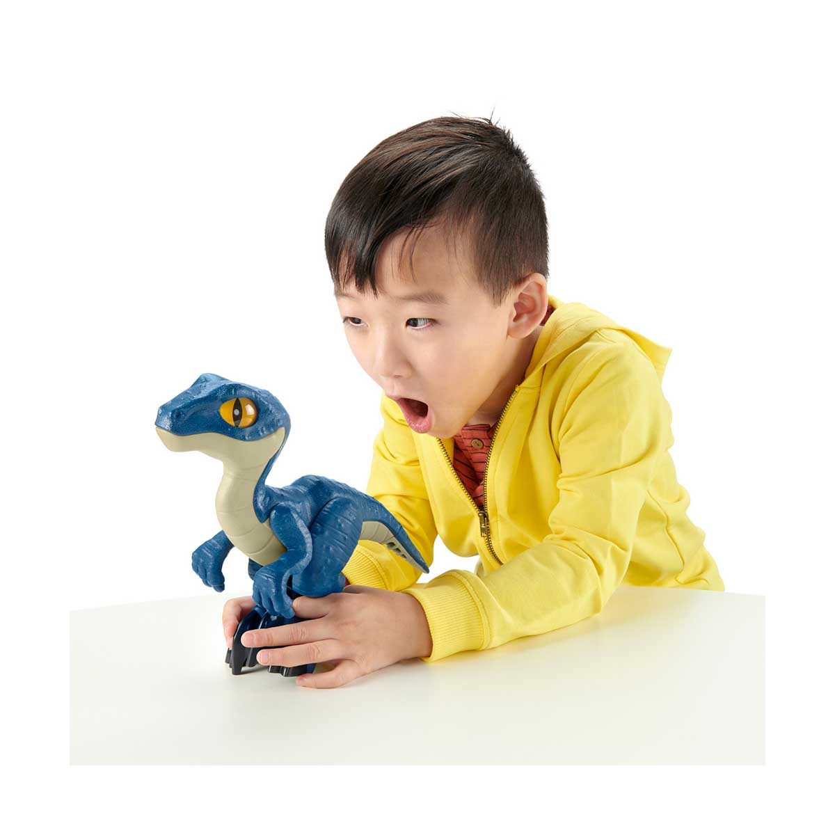 Ein Kind betrachtet ein blaues Dinosaurierspielzeug auf einem weißen Tisch, weißer Hintergrund.