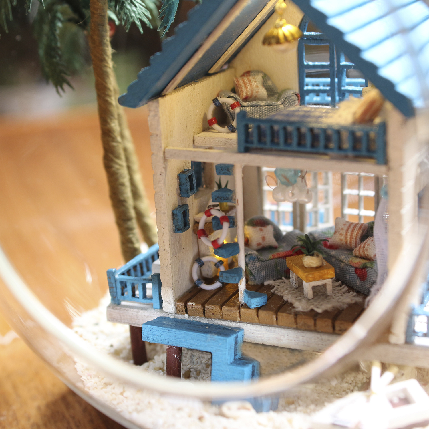 Casa sulla spiaggia in miniatura con dettagli blu, sabbia e palma. Dettagli interni visibili.
