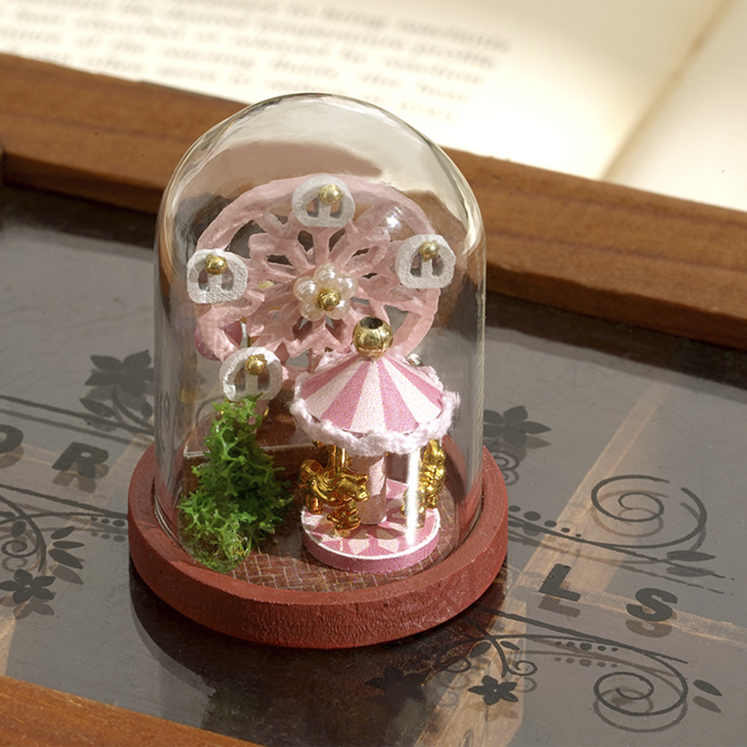 Giostra e ruota panoramica rosa in miniatura all'interno di una cupola di vetro. Su una base di legno. Sfondo sfocato.