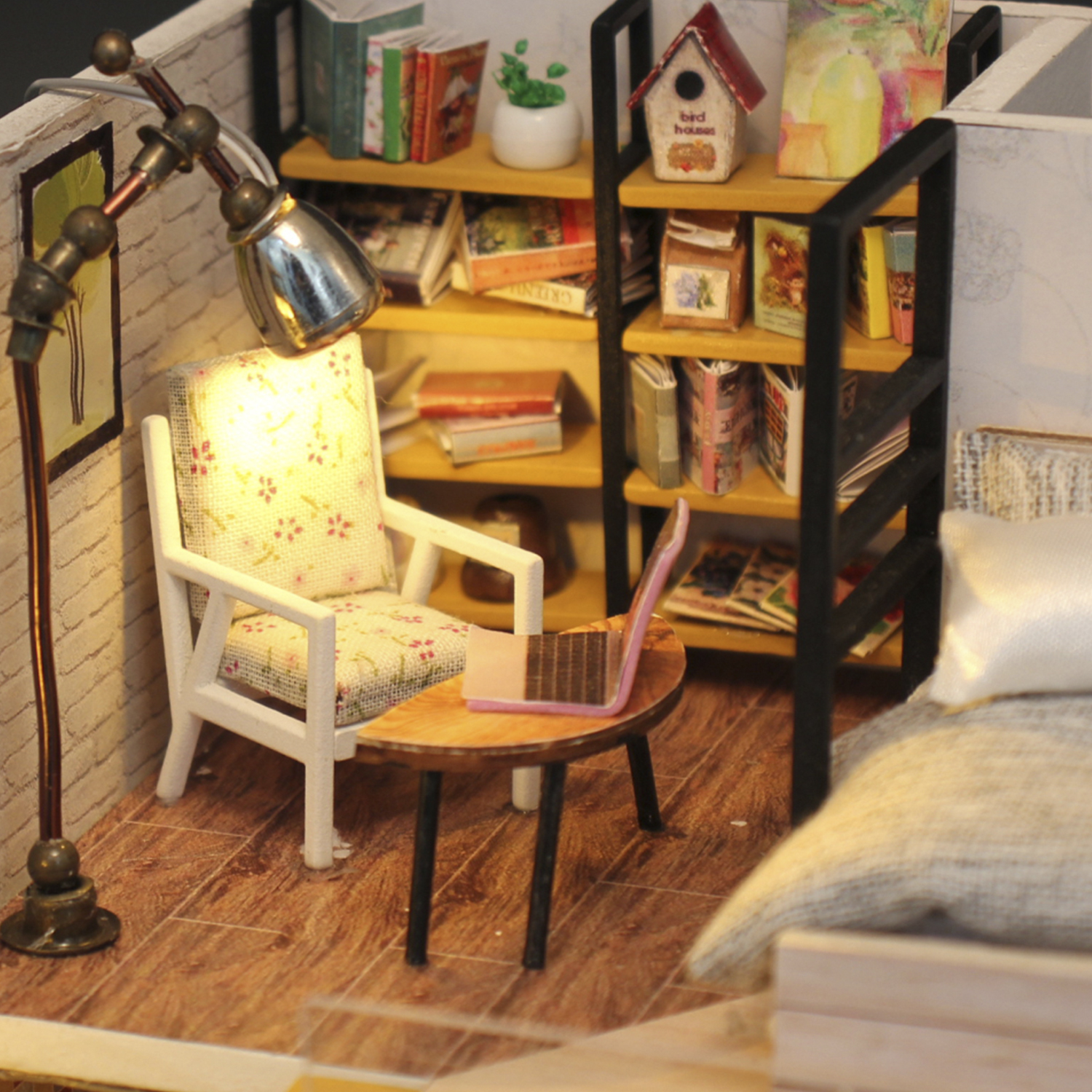 Stanza in miniatura con sedia, tavolino con laptop, librerie, lampada e letto.