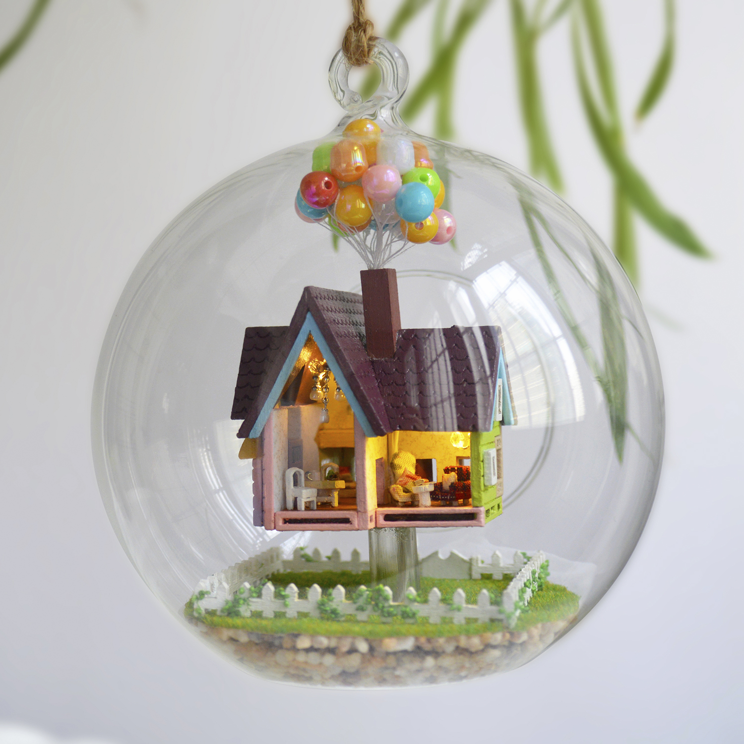 Una casa in miniatura galleggia all'interno di una palla di vetro. Palloncini sono attaccati.