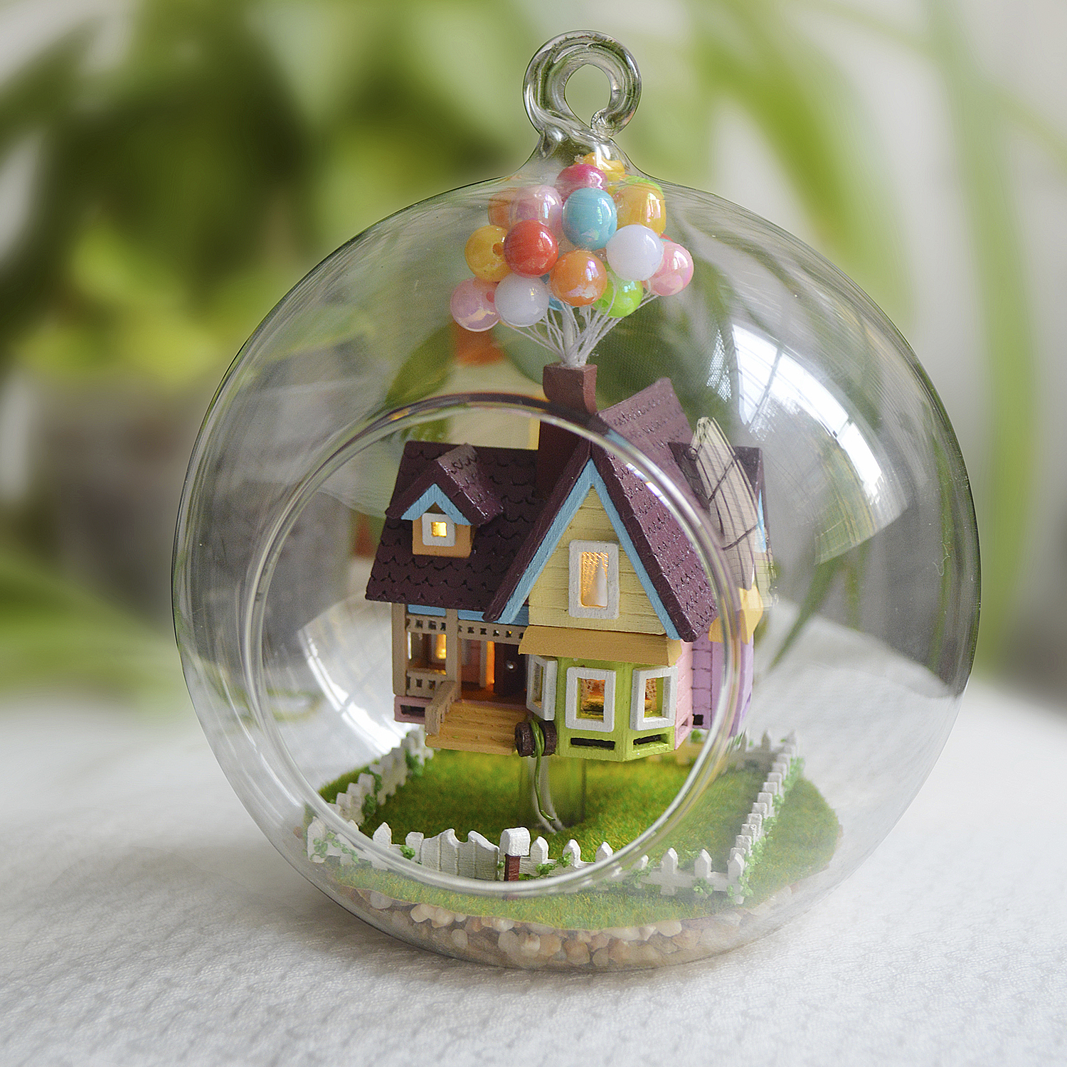 Casa in miniatura dentro una palla di vetro con palloncini sopra.