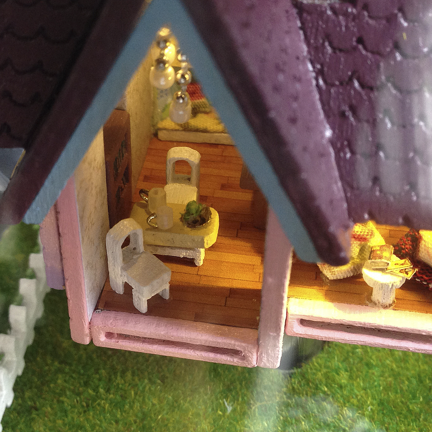 Interno di una stanza di casa delle bambole, con mobili e illuminazione in miniatura. Mostra un tavolino e sedie.