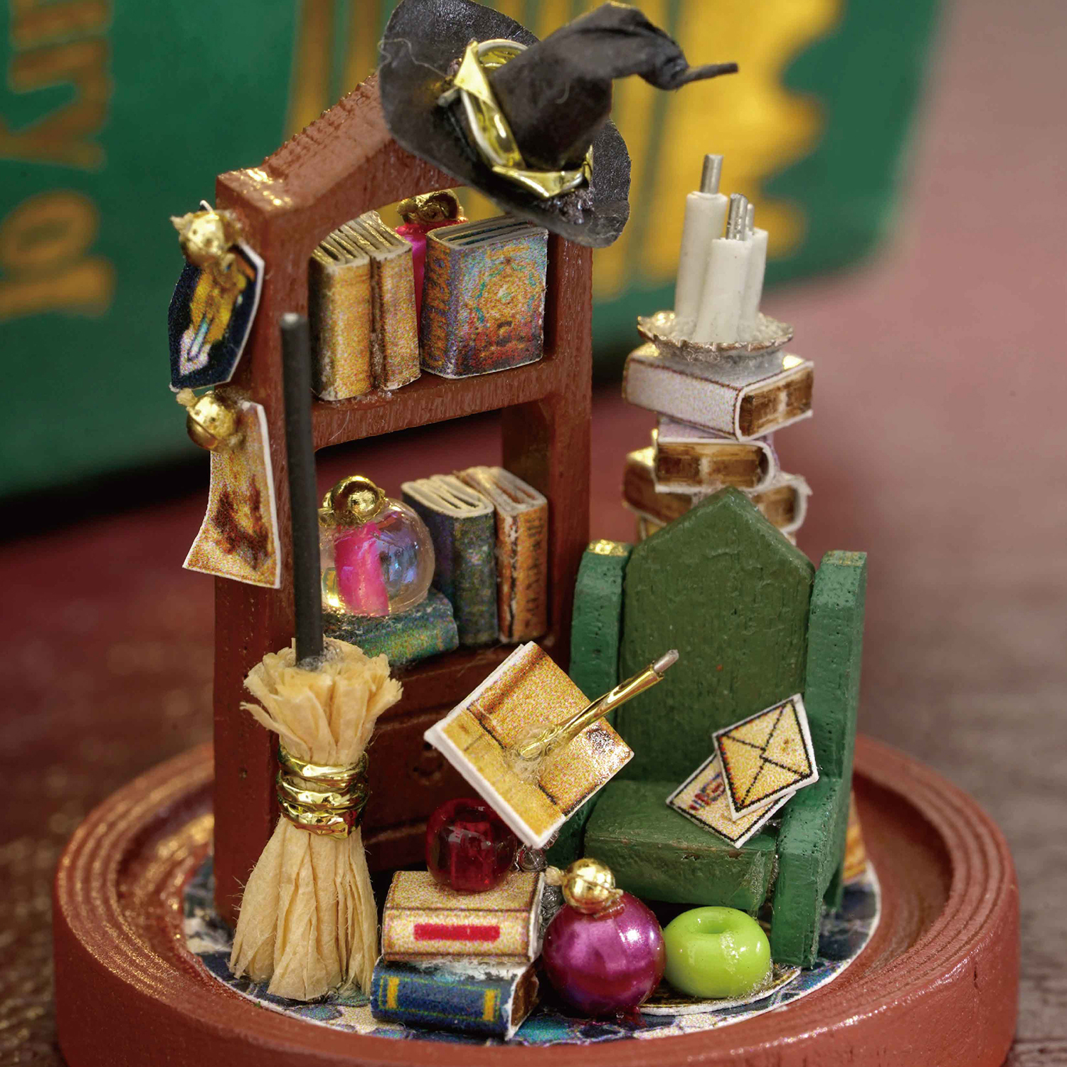 Stanza della strega in miniatura con libri, cappello, scopa e sedia verde su base rotonda.