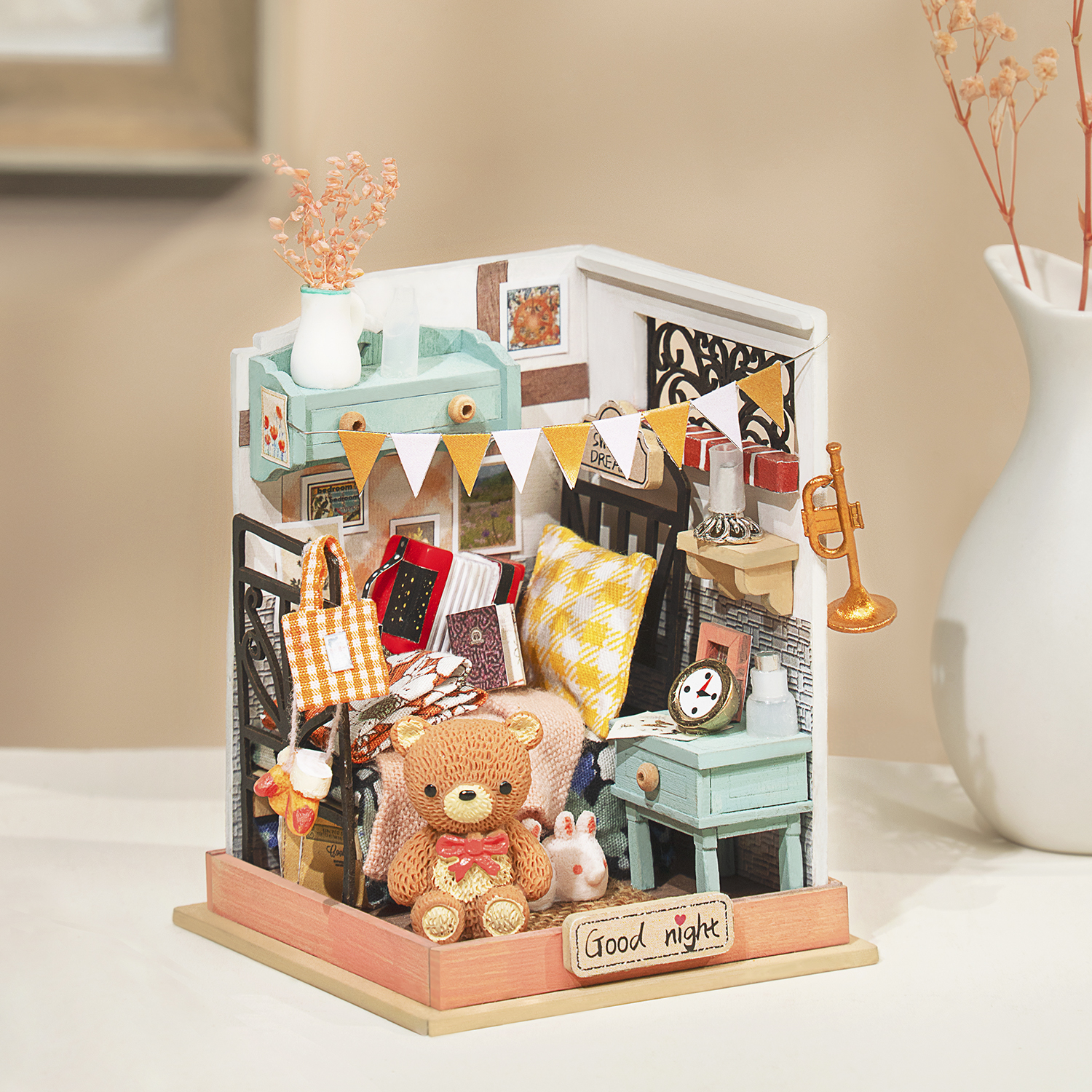 Diorama di una camera da letto in miniatura con letto, orsacchiotto e accessori, con un vaso bianco.
