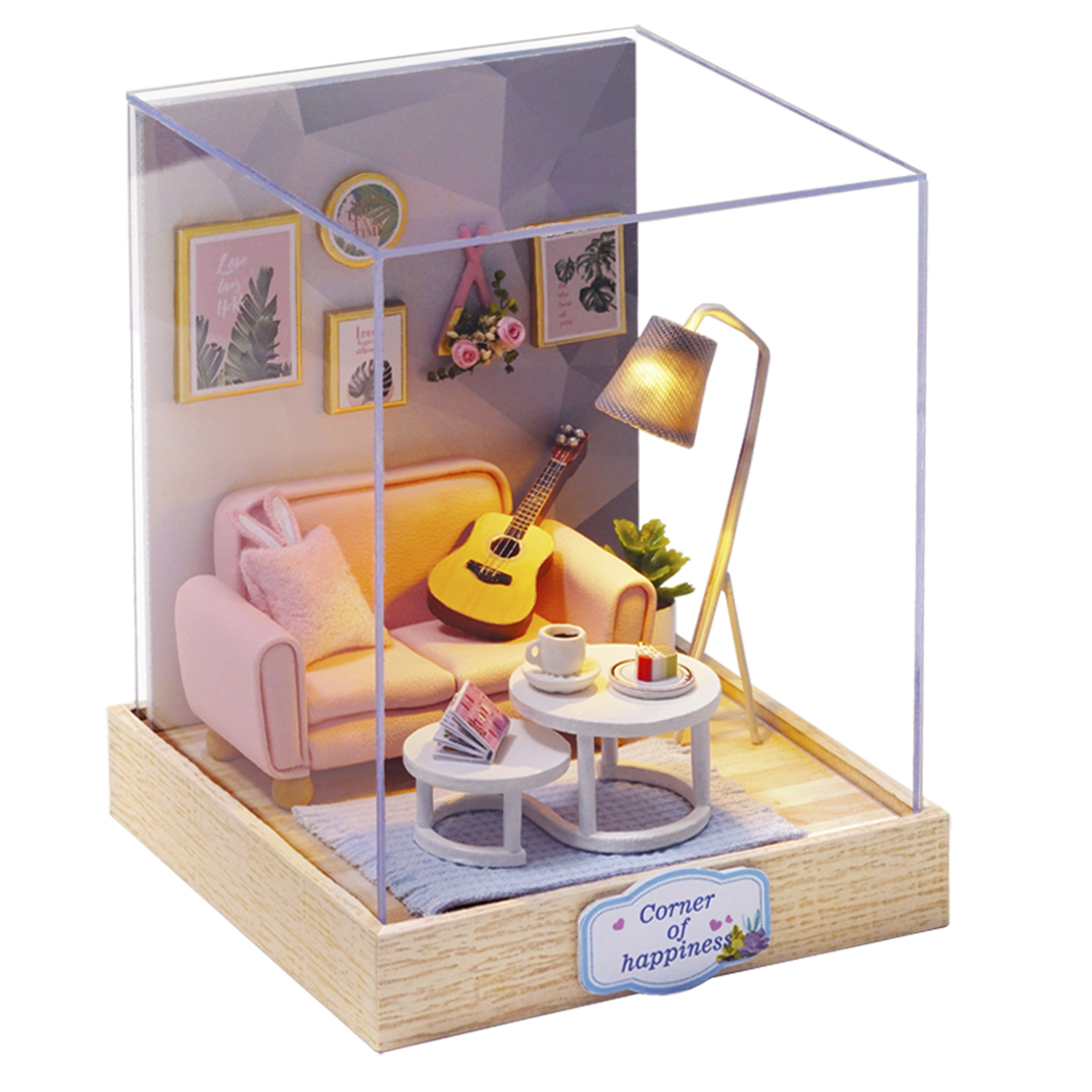 Scena di stanza in miniatura con divano rosa, chitarra e tavolini dentro una scatola trasparente.