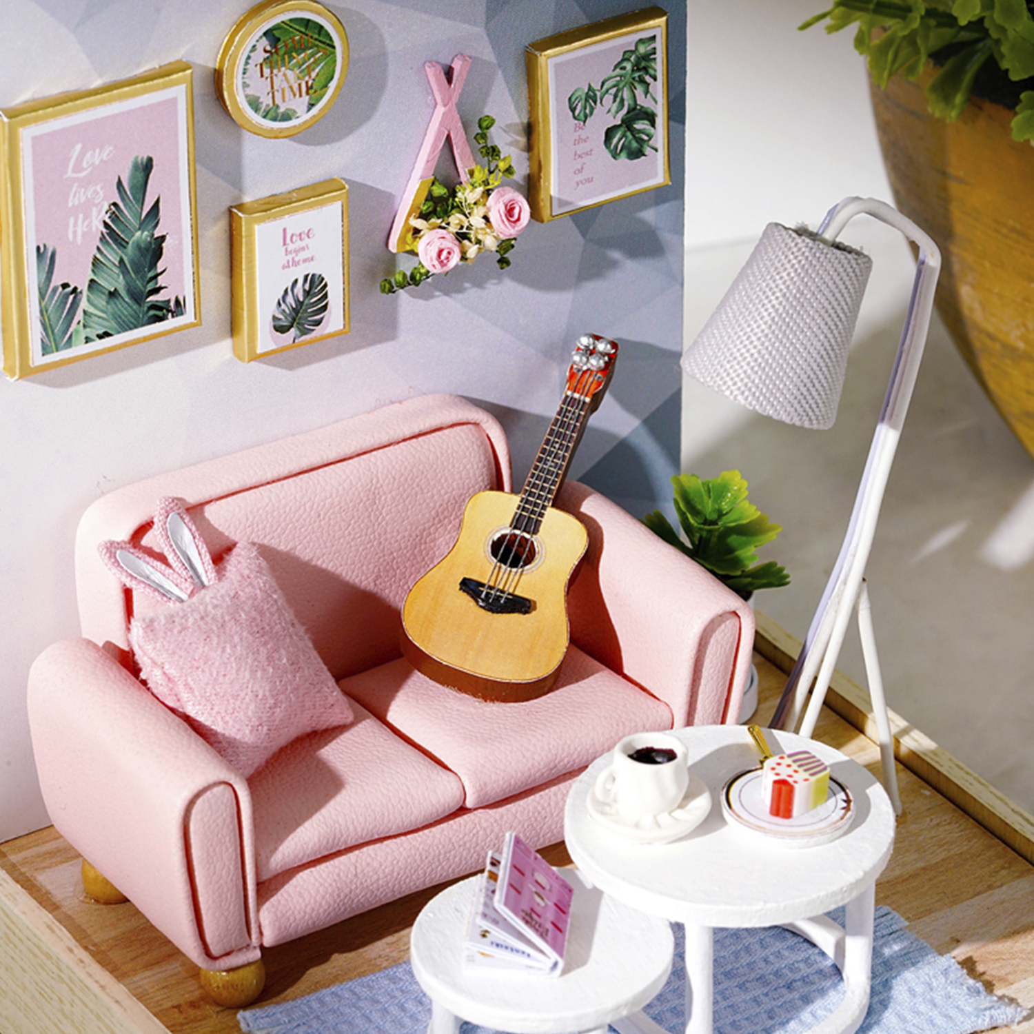 Scena di soggiorno in miniatura con divano rosa, chitarra, quadri sul muro e lampada.
