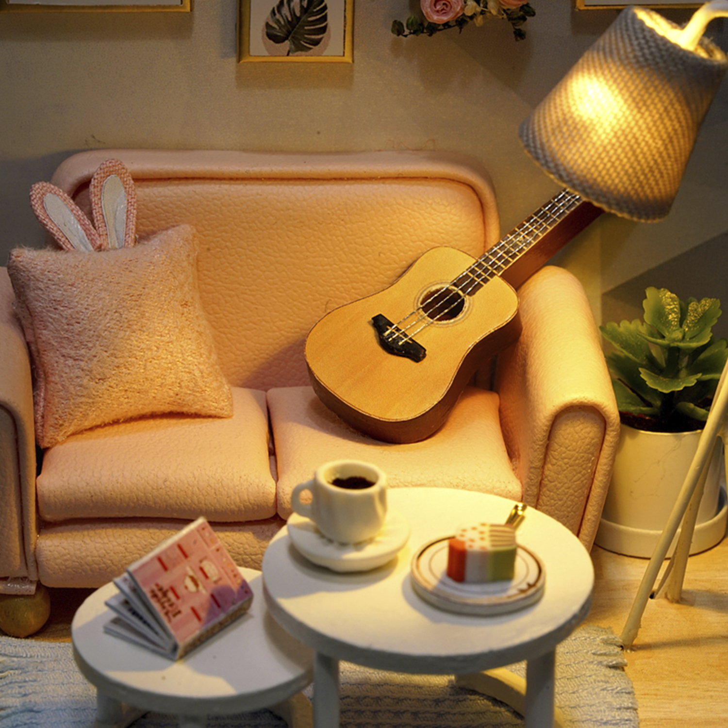 Una stanza in miniatura con un divano rosa, una chitarra e un tavolo con torta e caffè.